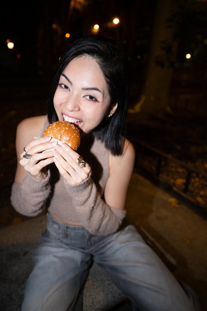 Hispanic woman eating burger on bench outdoors at night in Madrid