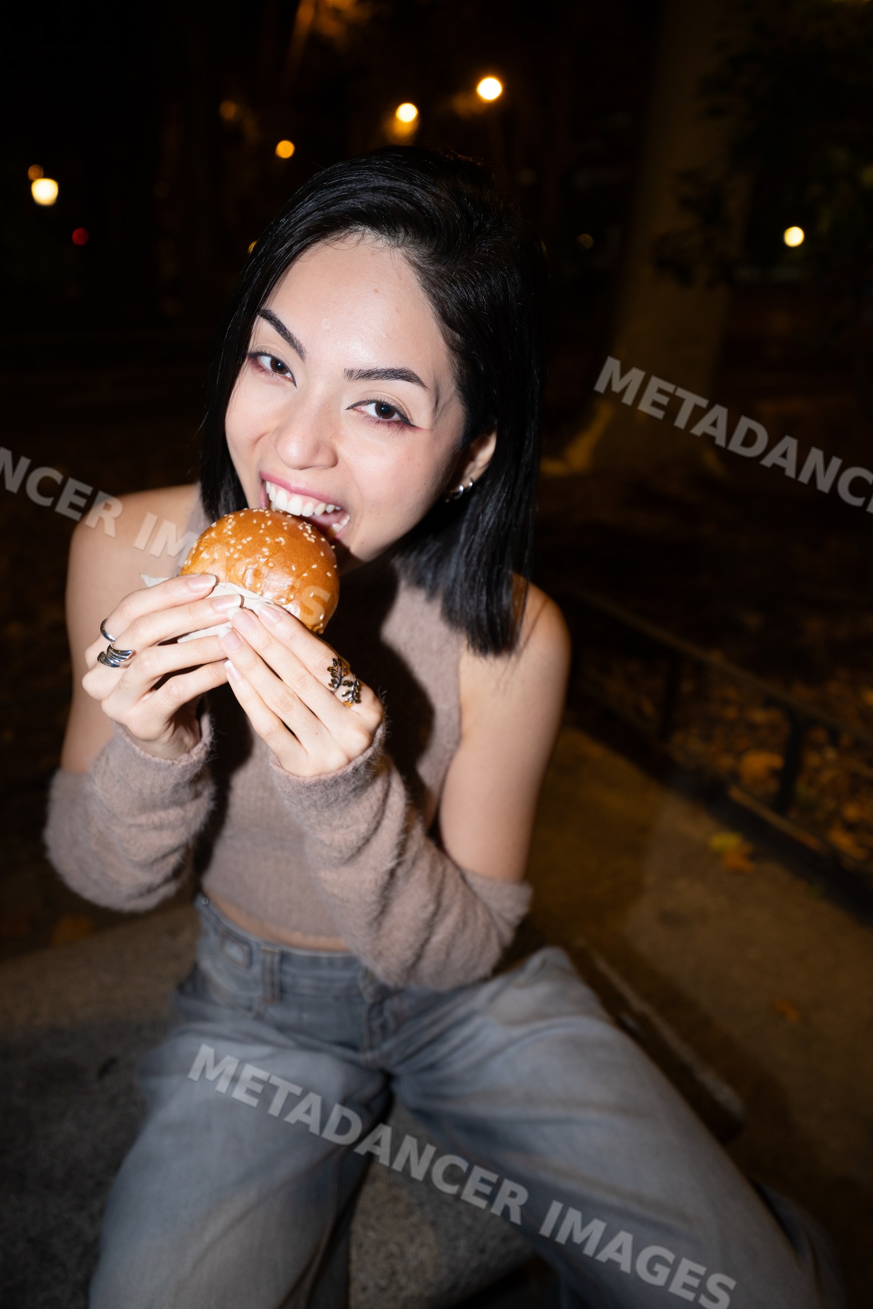 Hispanic woman eating burger on bench outdoors at night in Madrid