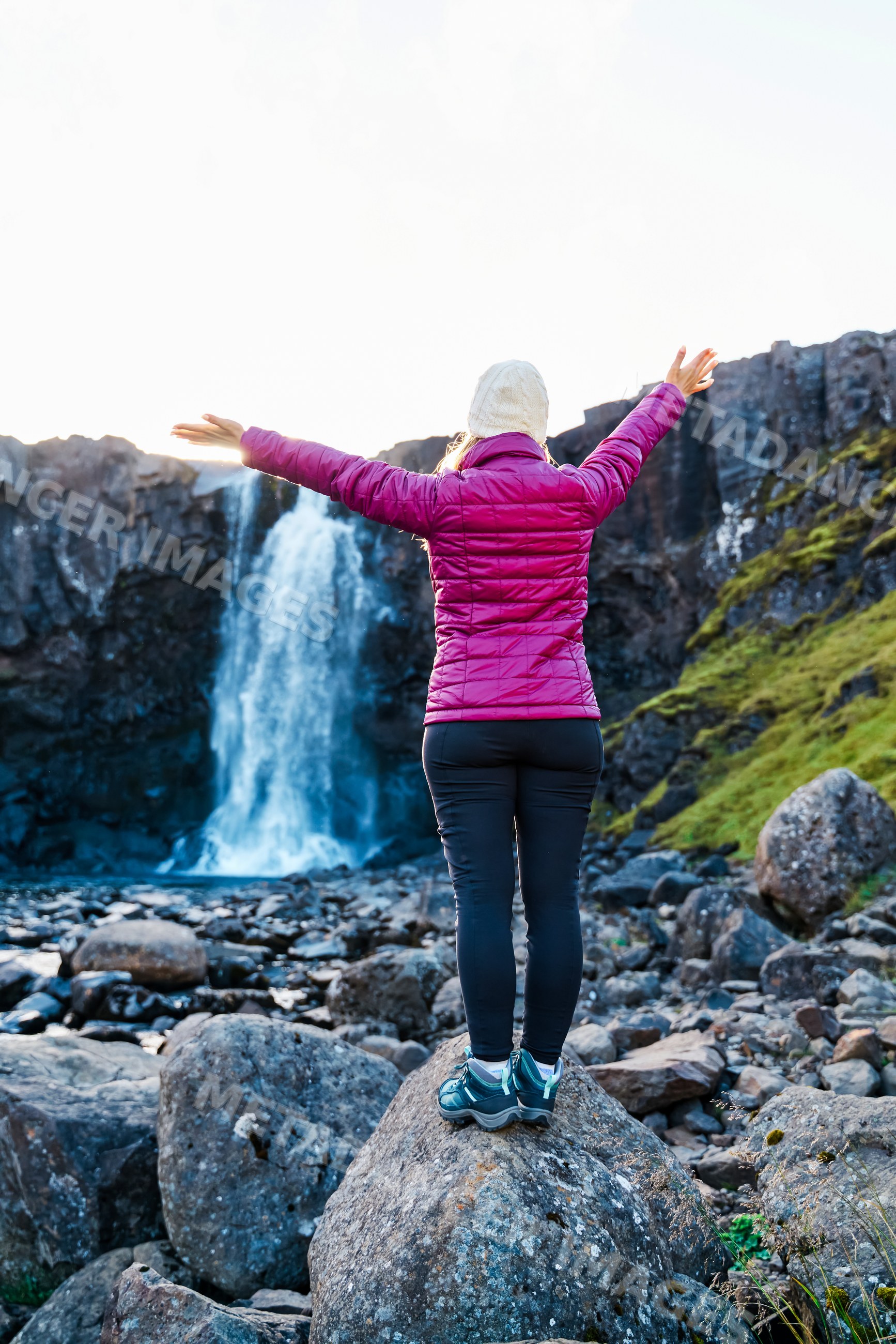 A white woman stands on a rock enjoying a waterfall