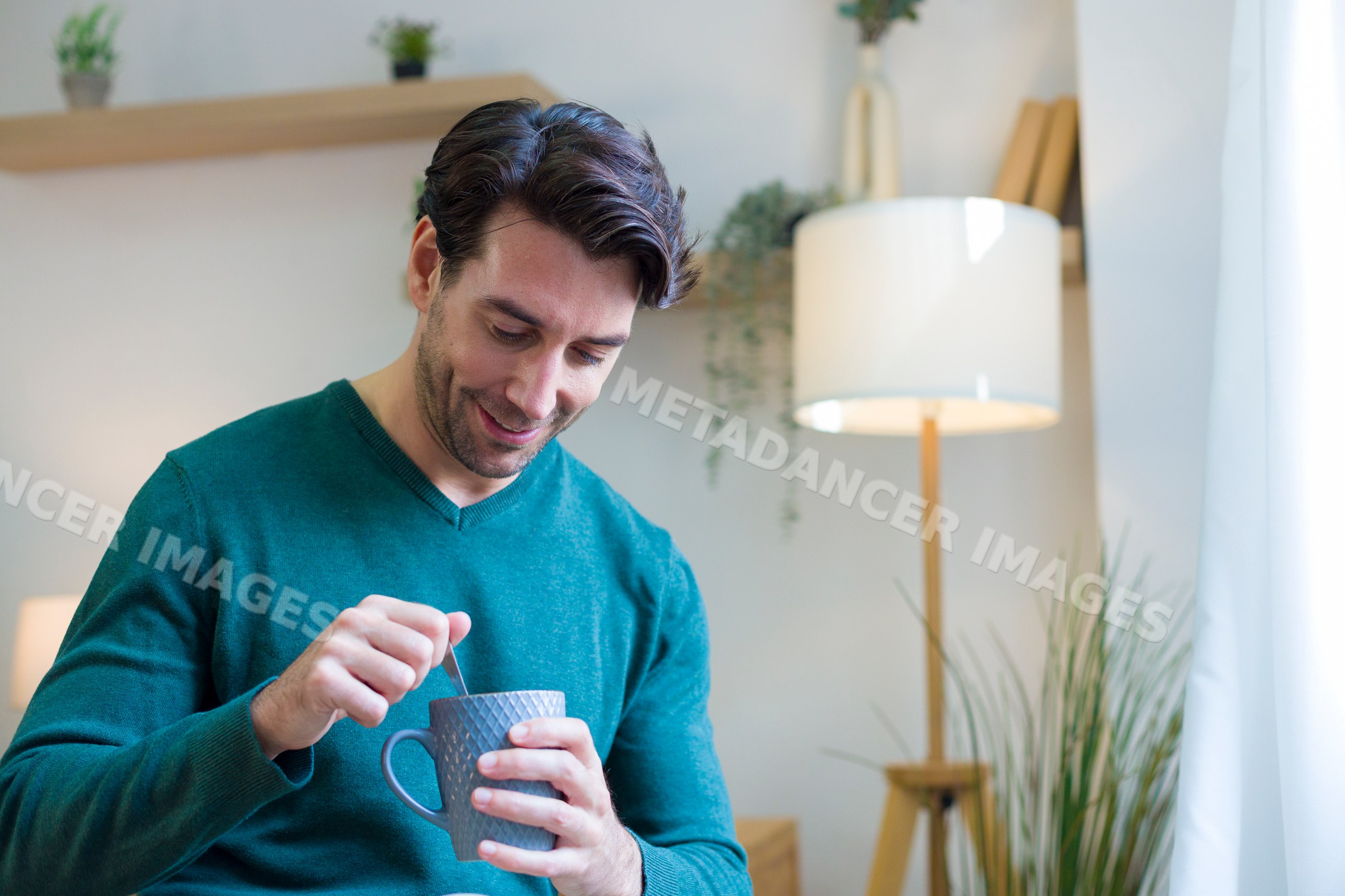 White man stirring drink in mug inside cozy home