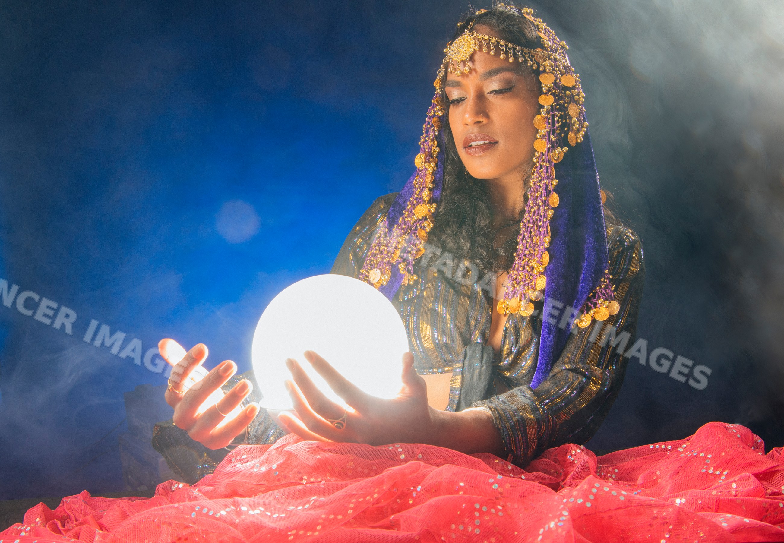 A South Asian woman holding a glowing crystal ball in a mystic setting