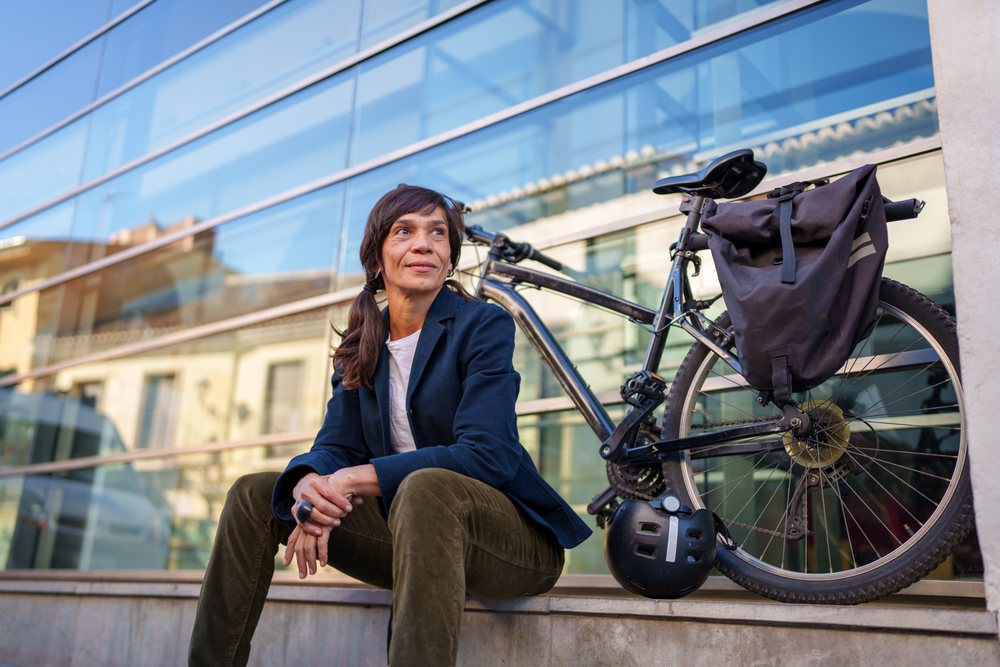 Hispanic woman sitting near bicycle by glass building in urban Málaga