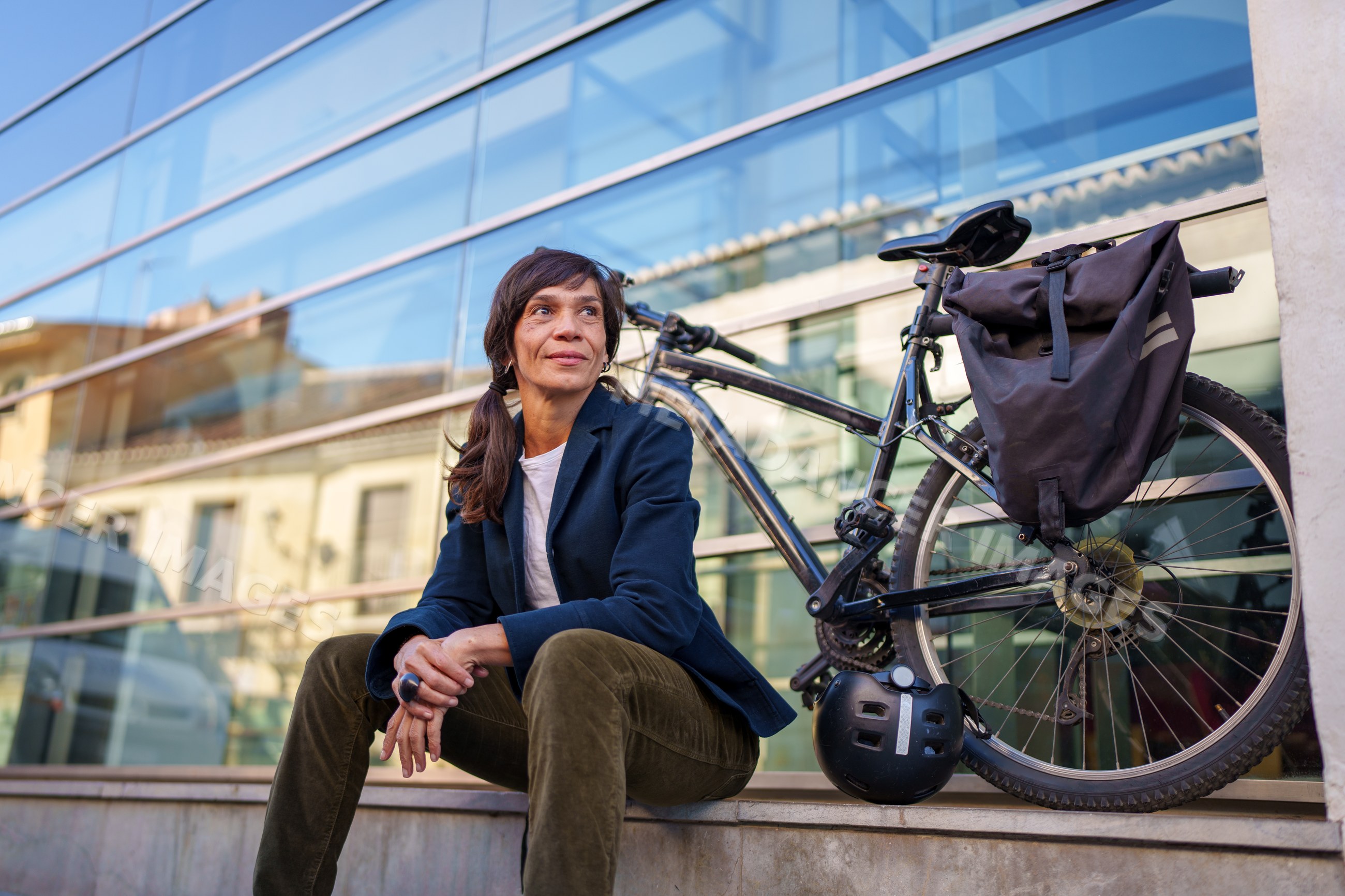Hispanic woman sitting near bicycle by glass building in urban Málaga