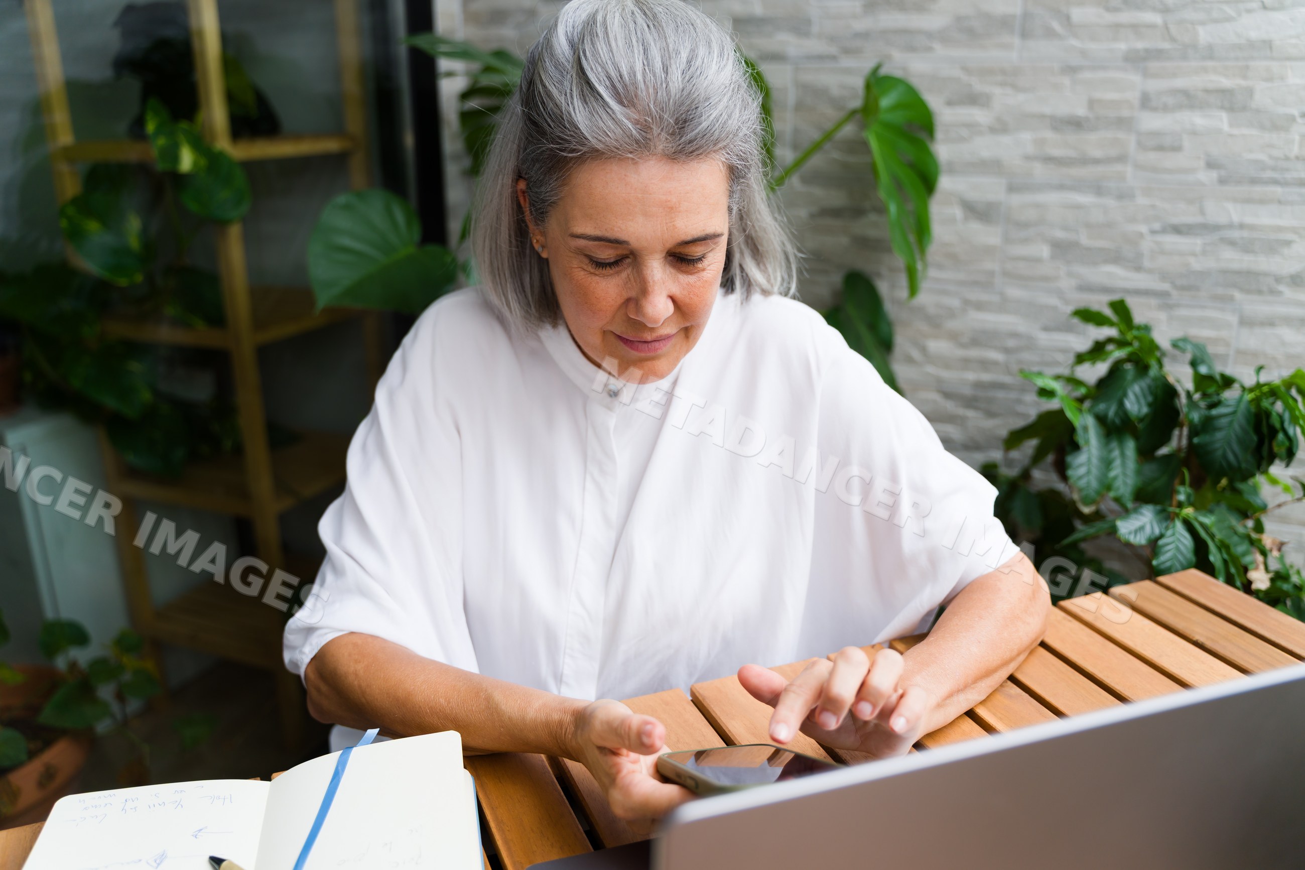 White Woman with gray hair using smartphone at wooden table indoors