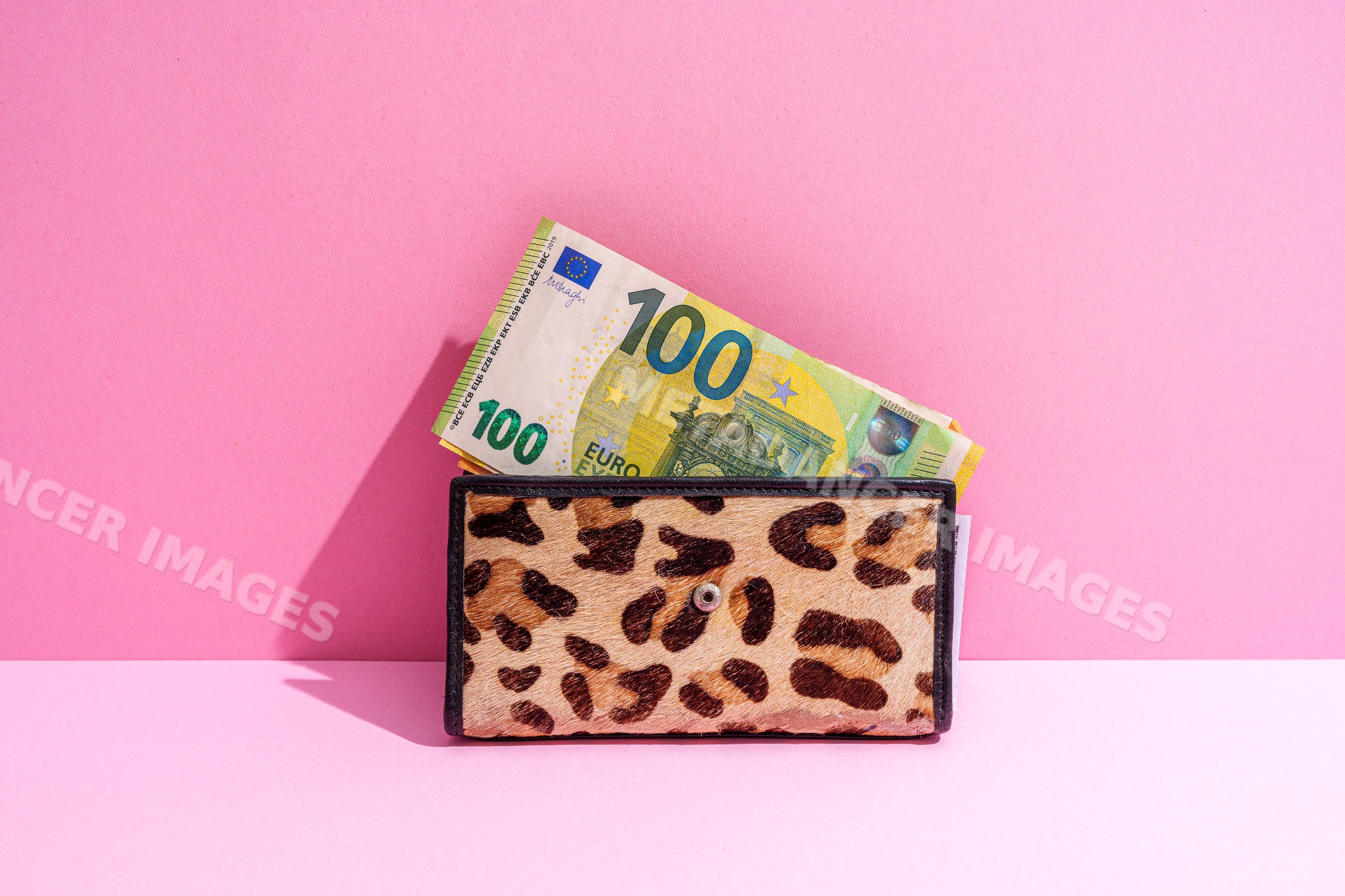 Leopard print wallet with hundred euro notes on pink background