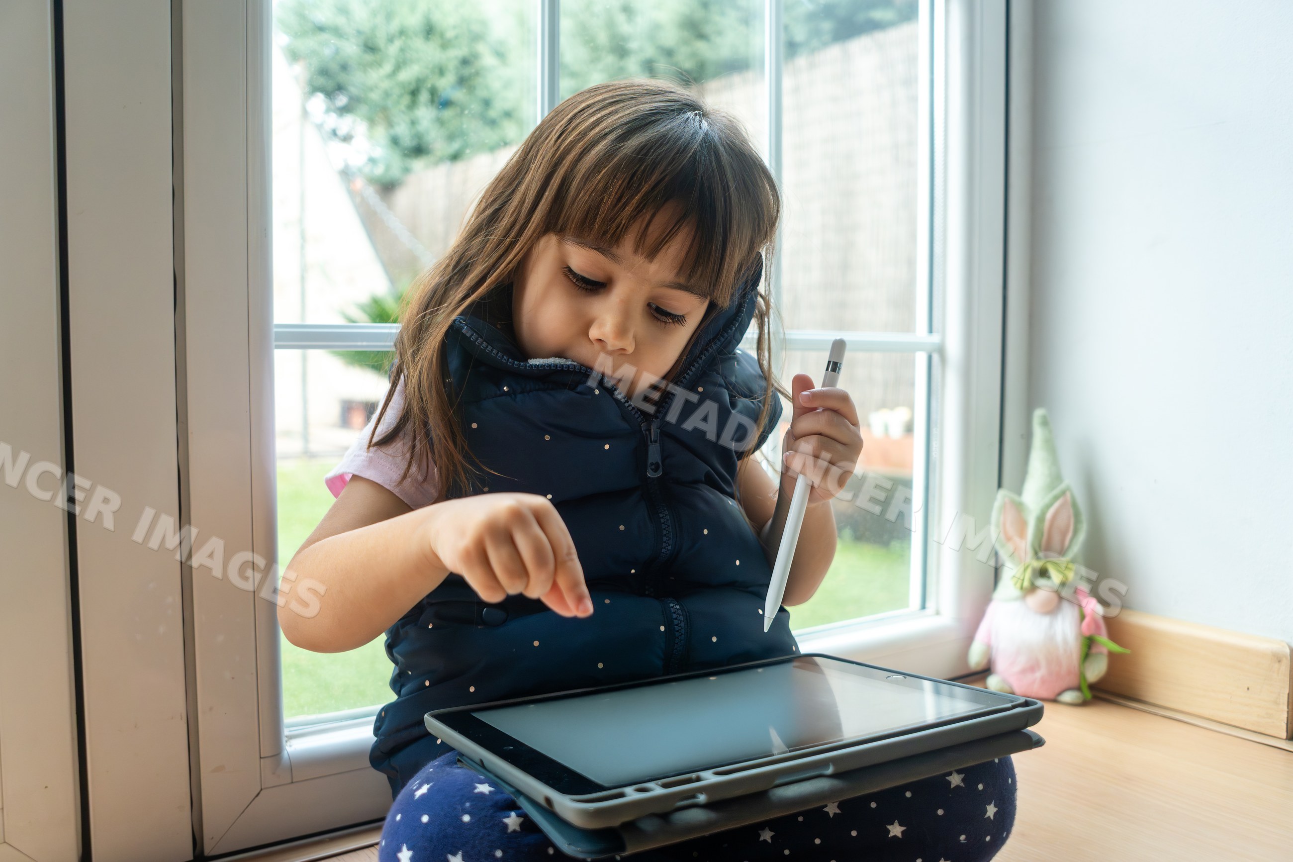 A young white girl uses a digital tablet with a stylus pen at home
