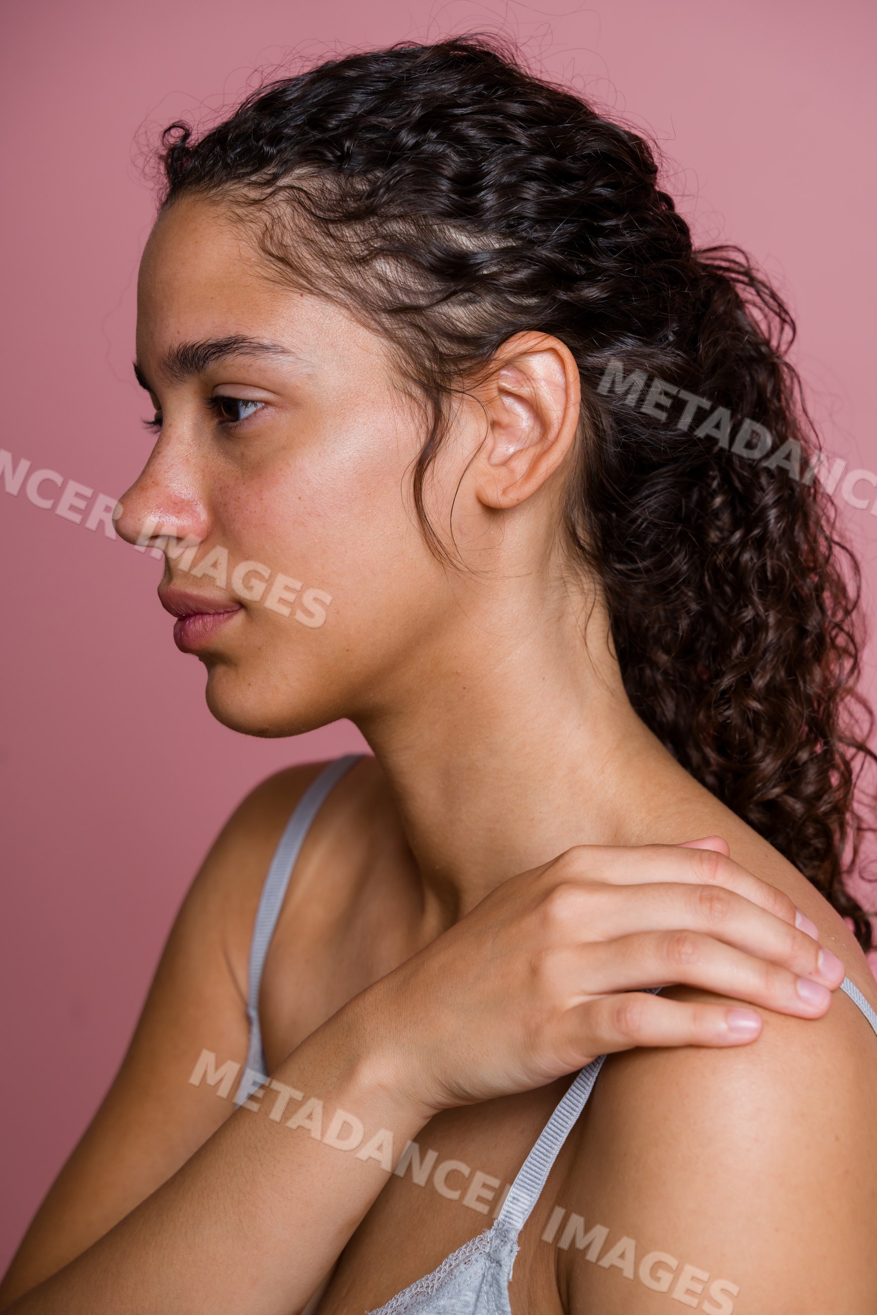 Profile of young Hispanic woman touching her shoulder with curly hair