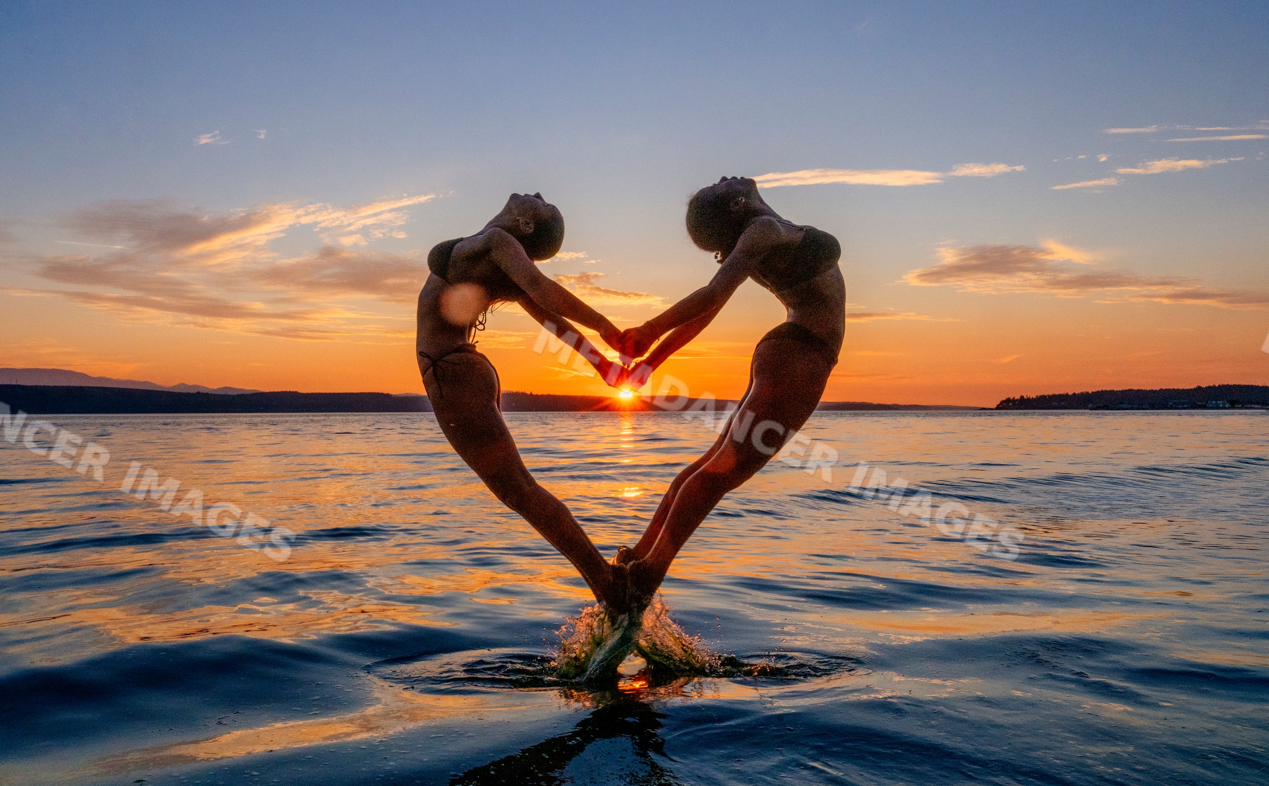 Two women performing partner acrobatics yoga at sunset on water