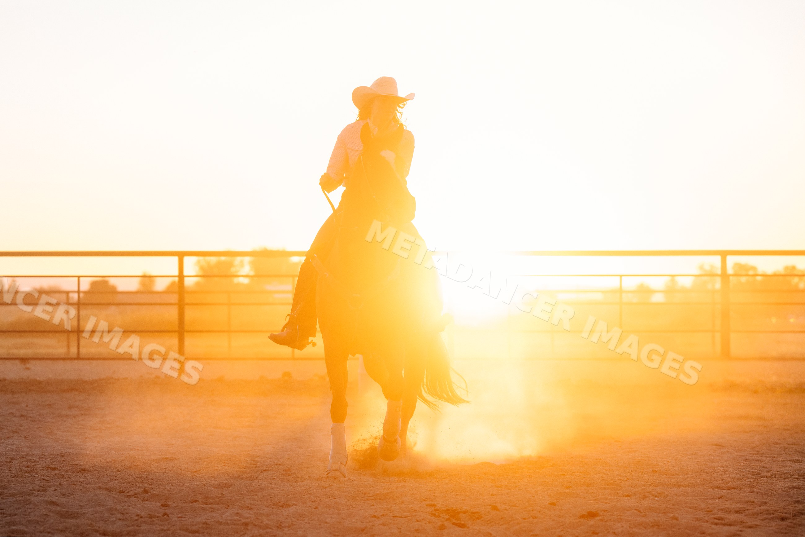 Horseback rider galloping through dusty outdoor arena at sunset