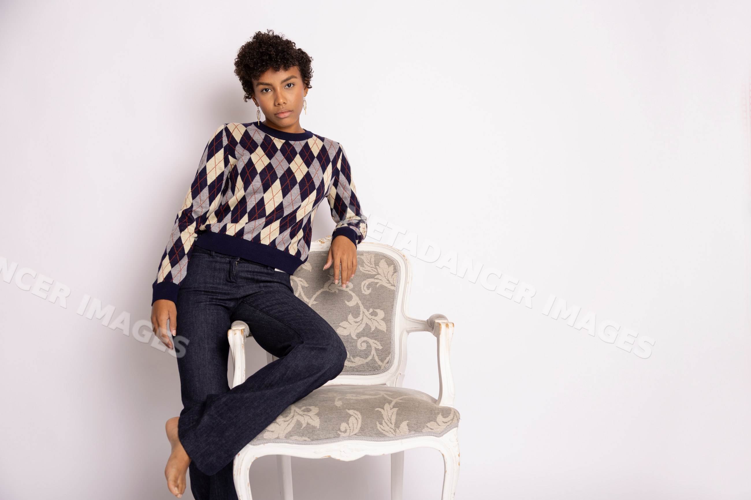 Hispanic woman in argyle sweater and blue jeans standing by armchair