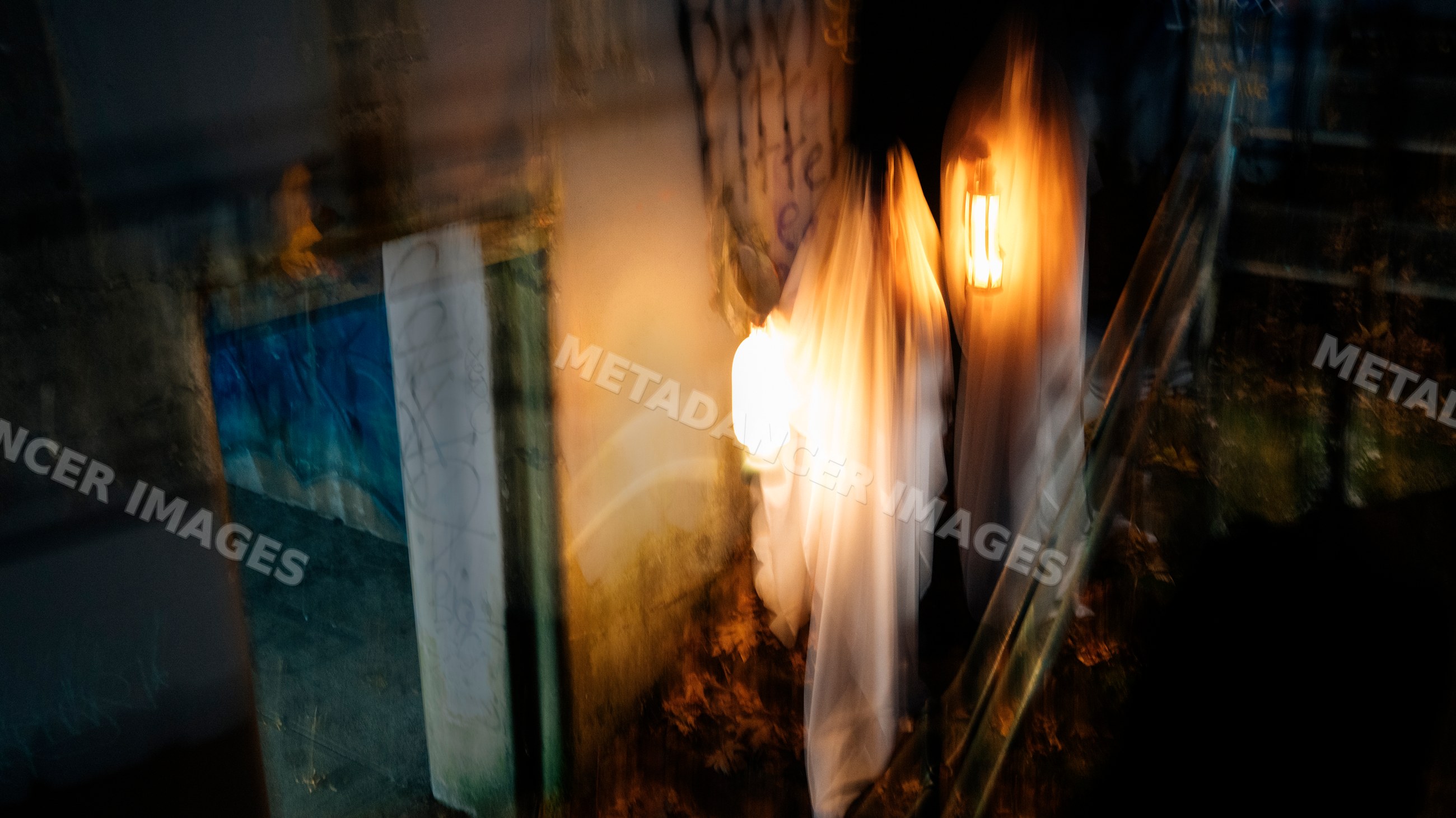 Two white people in ghost costumes holding a lantern in a dark hallway