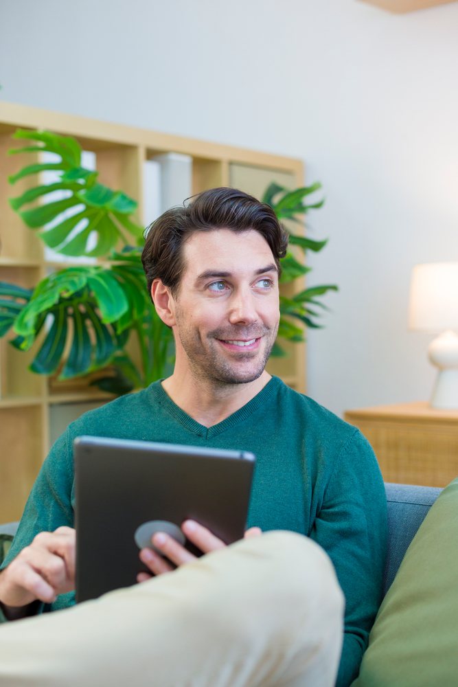 White man sitting on couch using tablet in living room