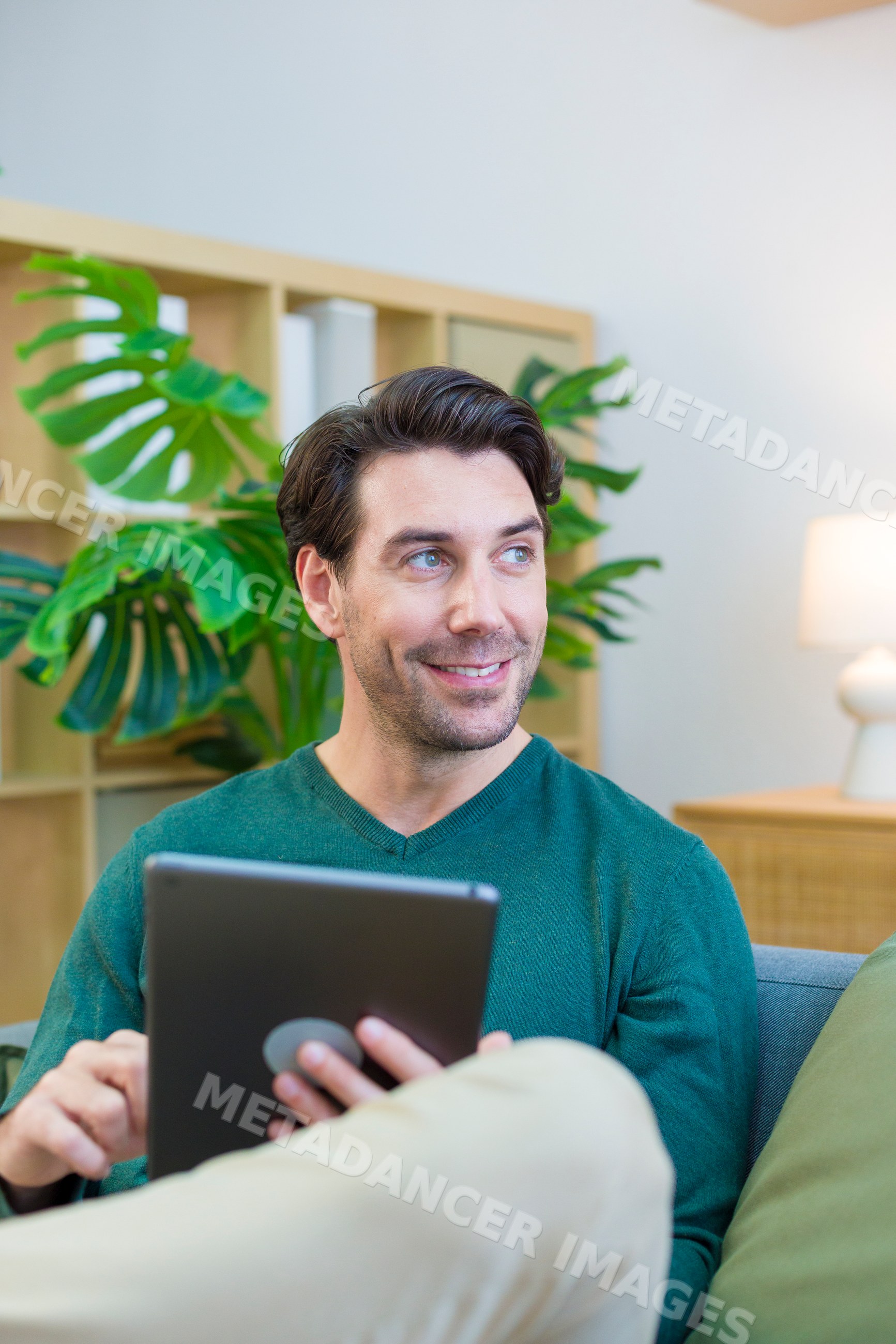 White man sitting on couch using tablet in living room