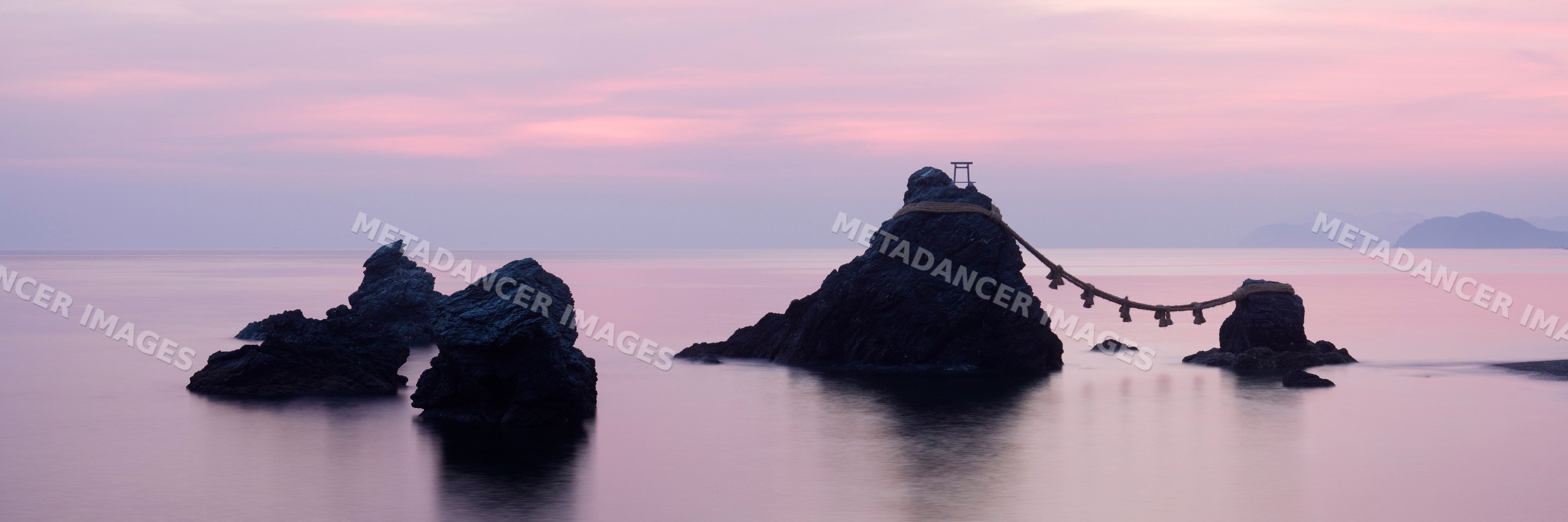 Rocks connected by shimenawa rope and torii gate at ocean dawn