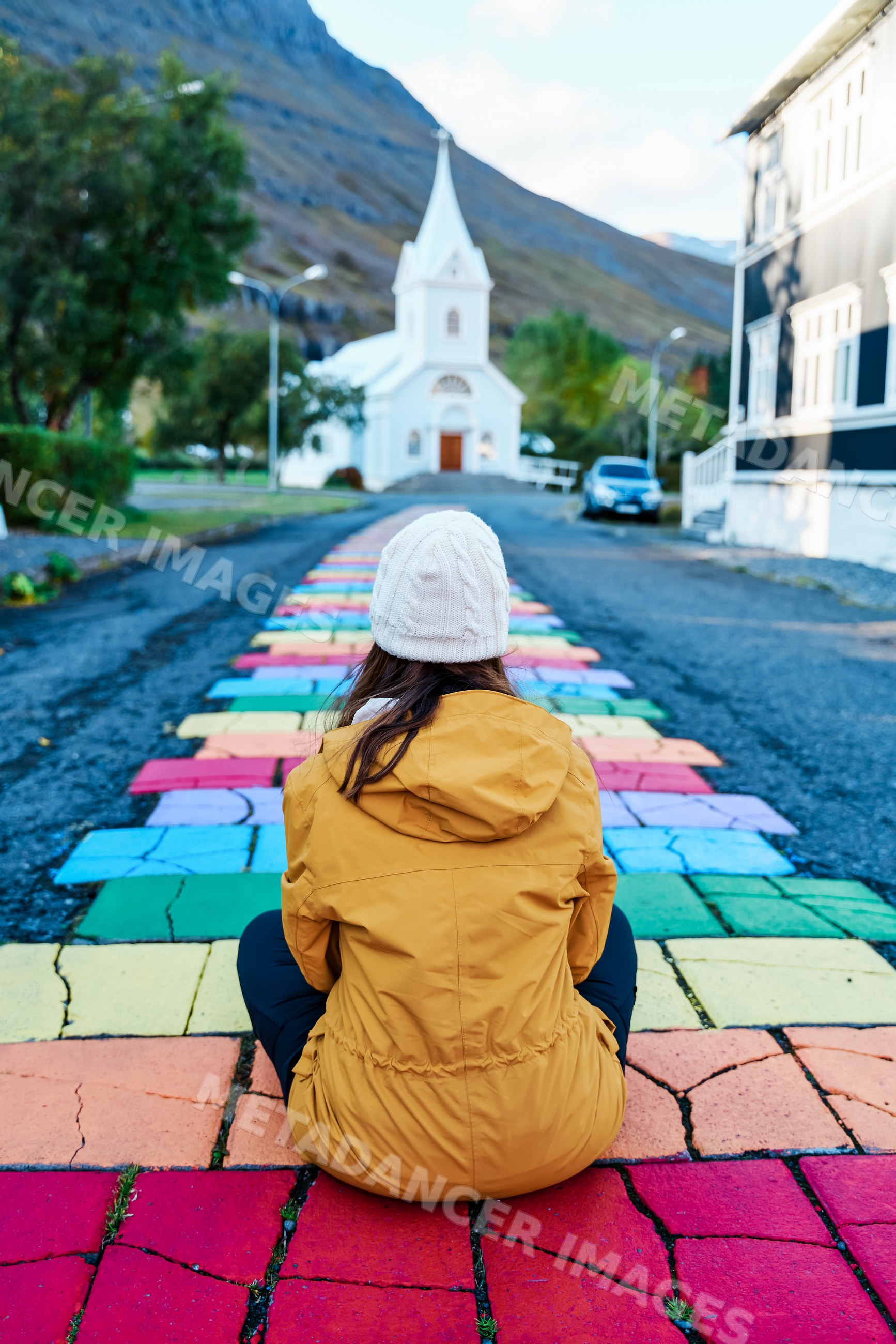 A white woman sits on a colorful path leading to a small church