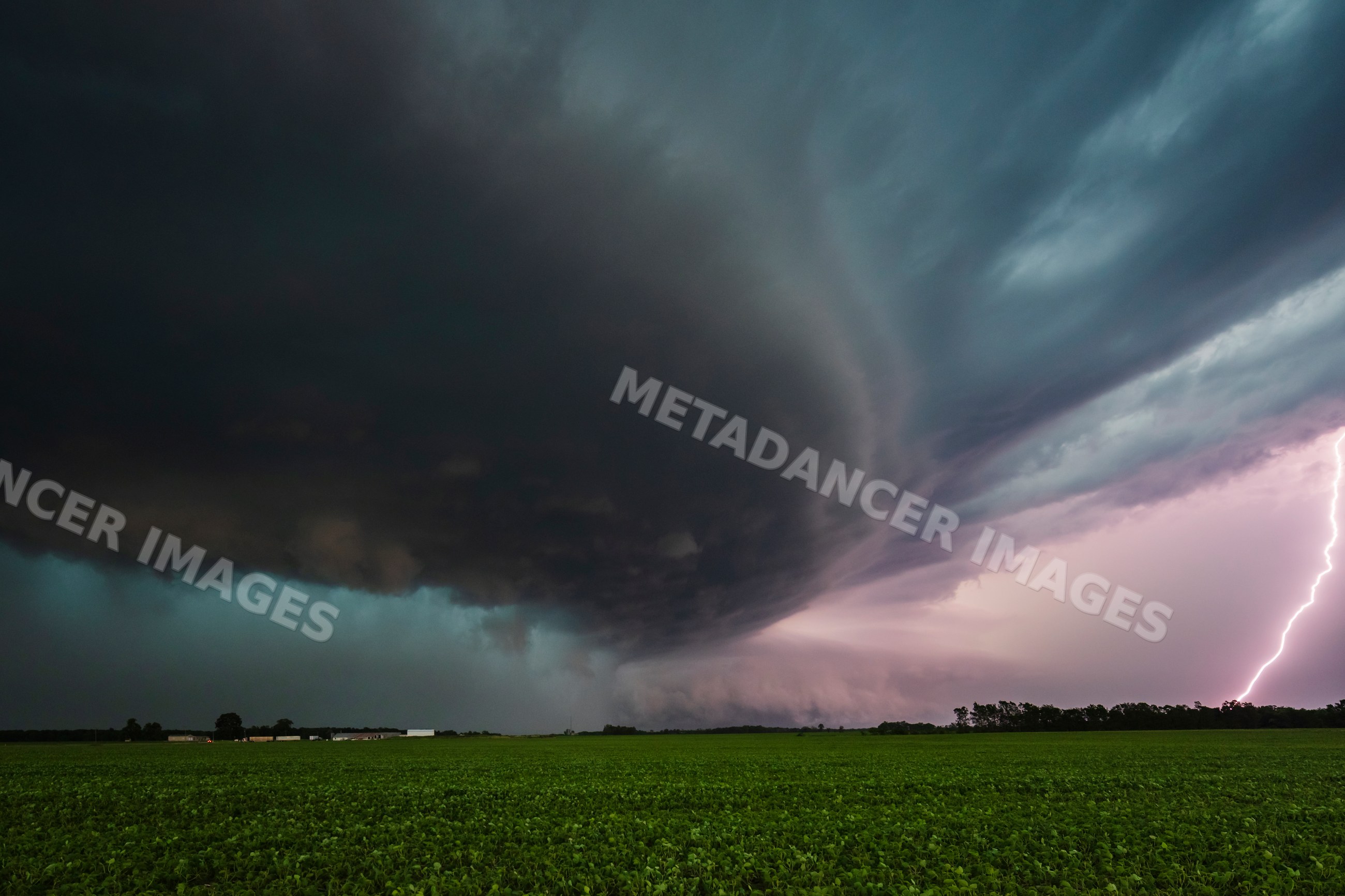 Supercell storm with lightning striking over a green field