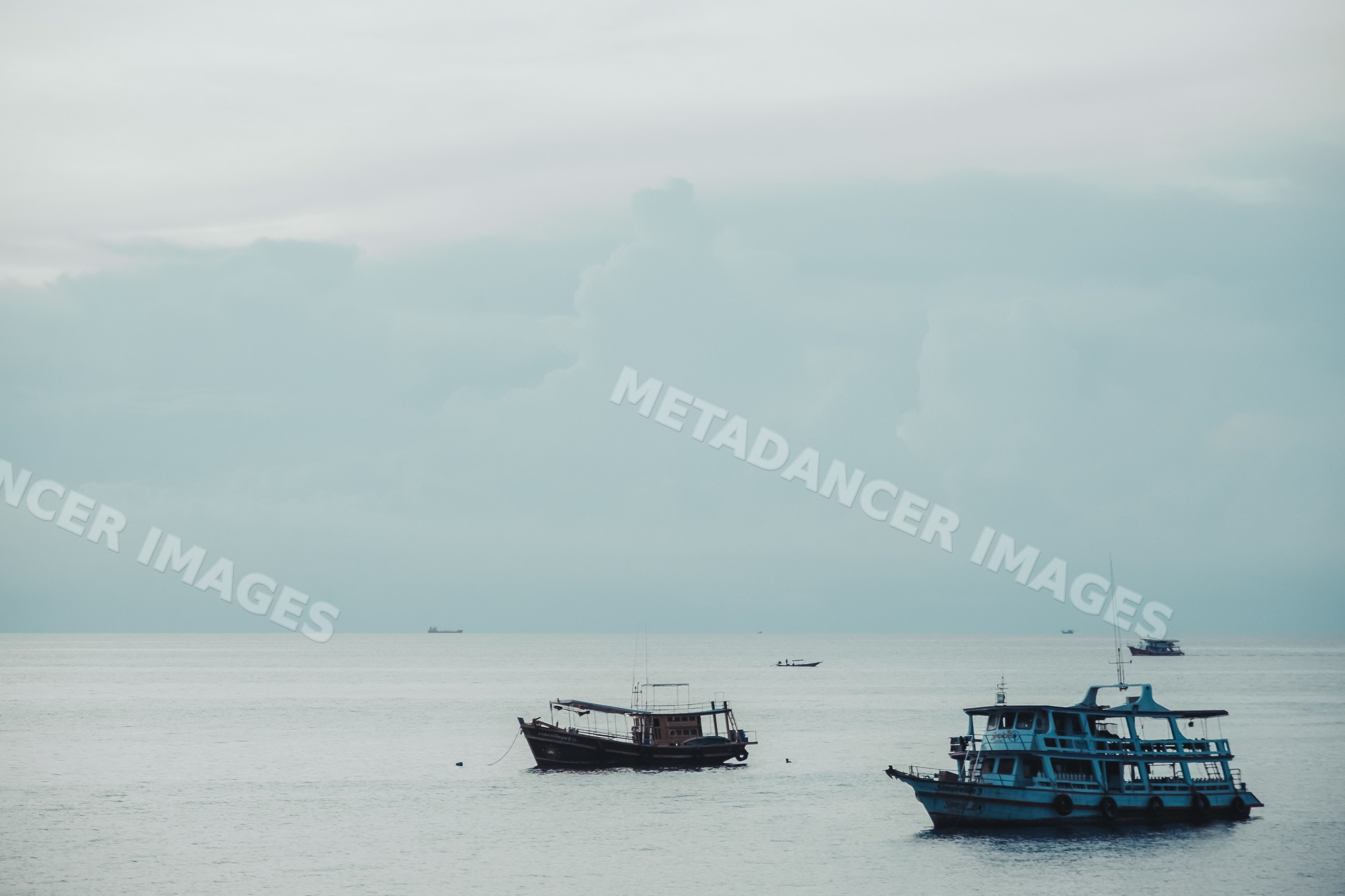 Fishing boats anchored on calm sea under cloudy sky