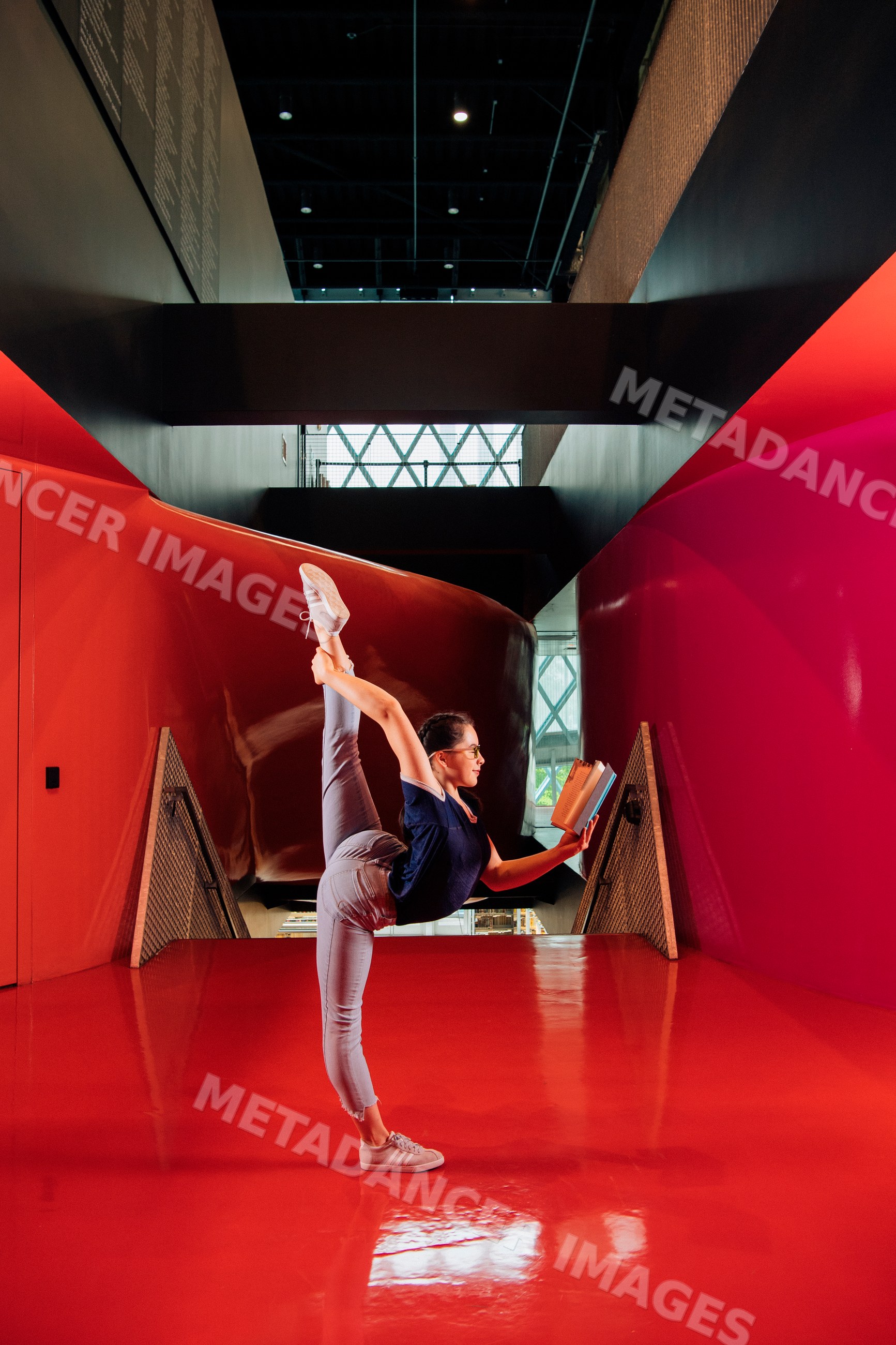 A young woman reads a book while doing a yoga stretch in a library