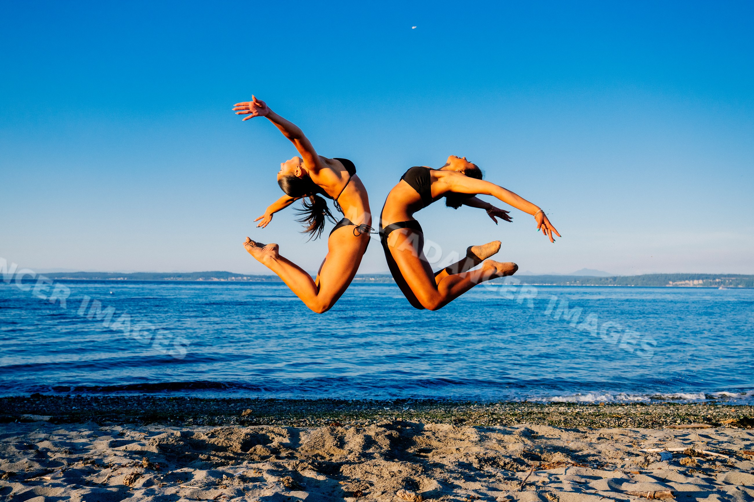 Two women jump in synchronized acrobatic motion on a beach in wa USA