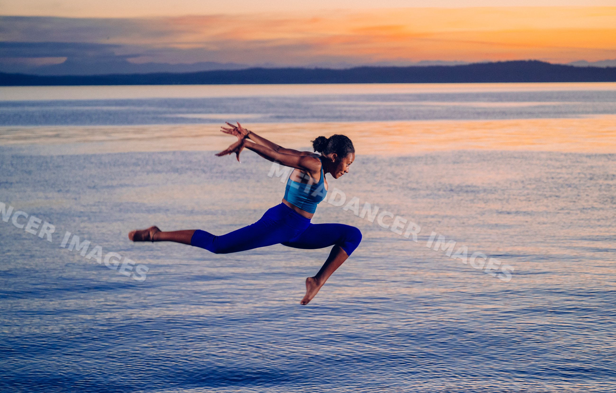 Hispanic woman performing a split jump exercise over lake at sunset