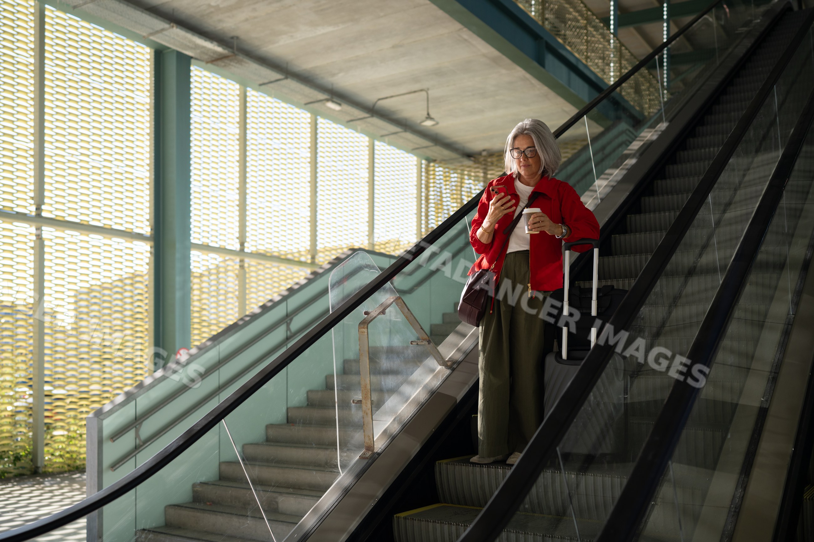 White woman using smartphone and holding coffee on indoor escalator