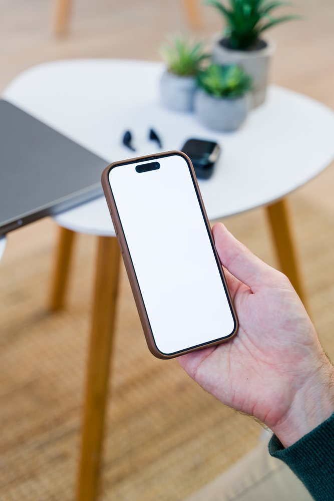 Smartphone held above white table with laptop and wireless earbuds