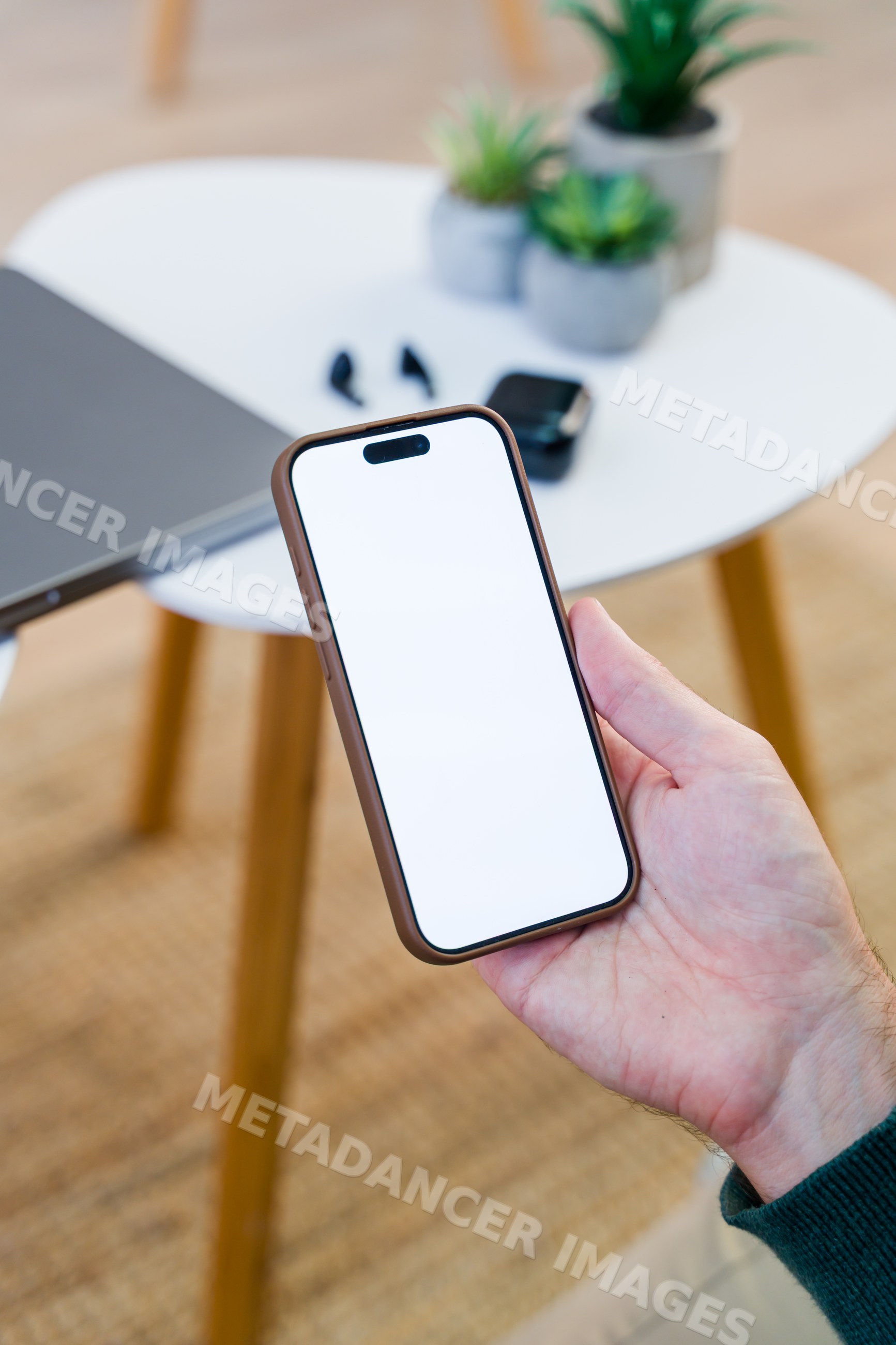 Smartphone held above white table with laptop and wireless earbuds
