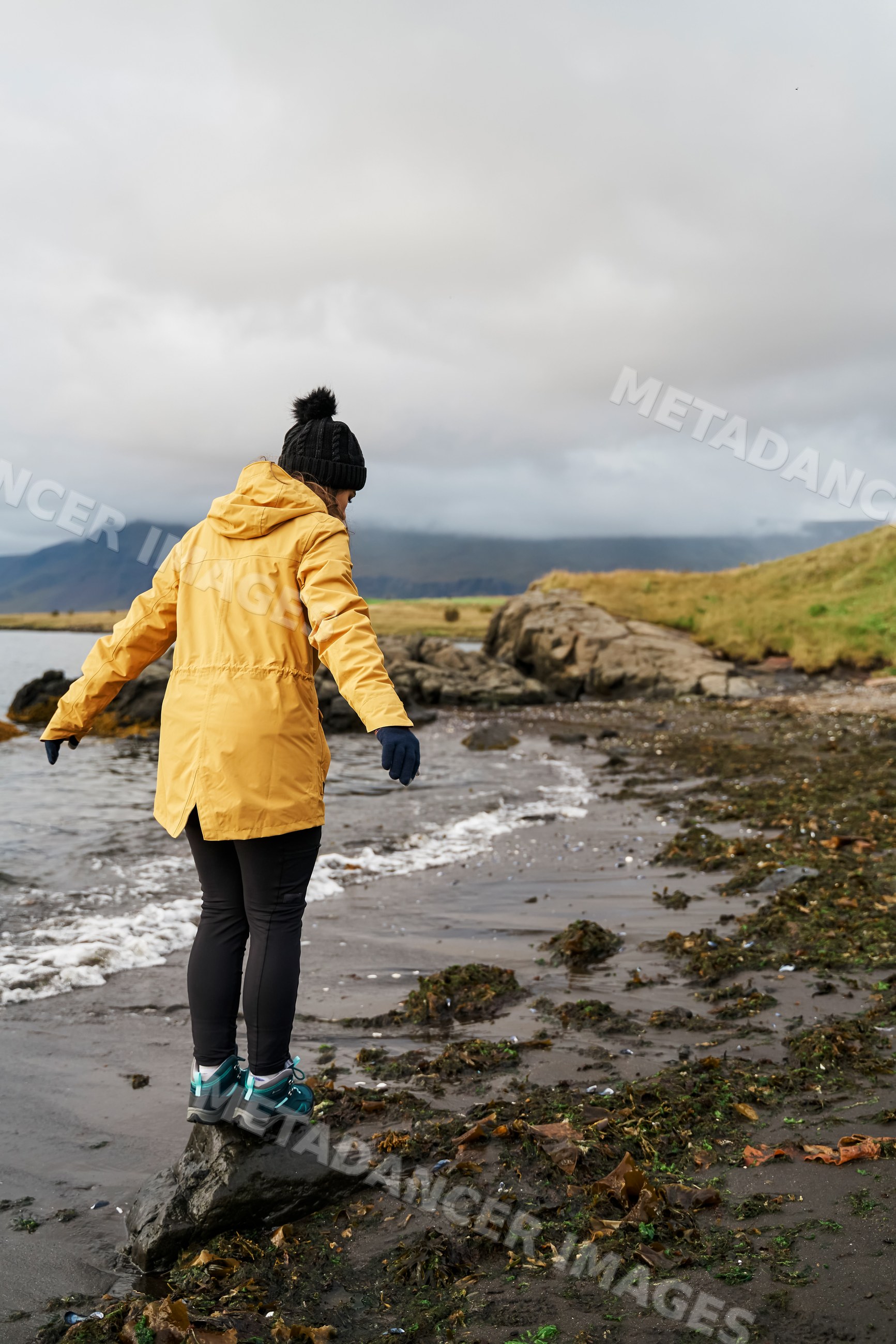 A white woman balances on a rock along the shoreline