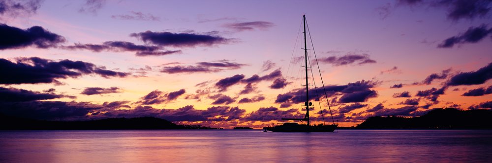 Yacht silhouette on calm ocean water at colorful sunset