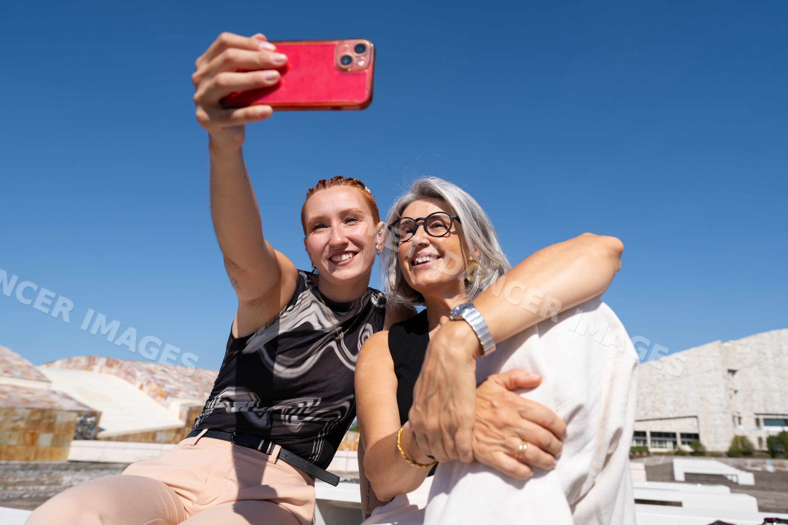 White women taking selfie outdoors with bright blue sky and modern