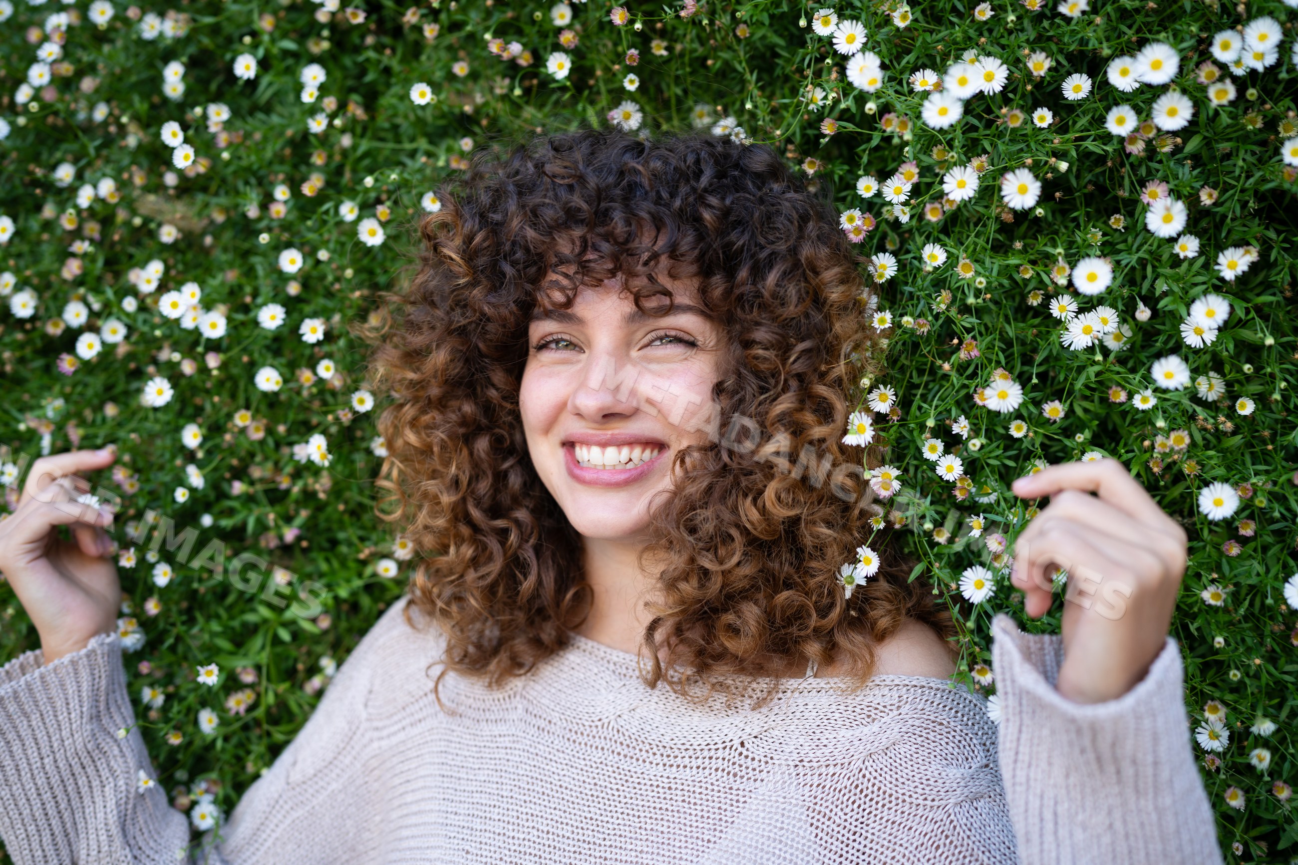 White woman with curly hair smiling in field of daisies outdoors