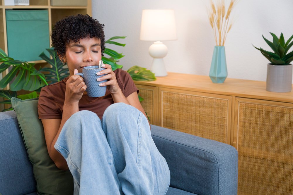 Young African American woman relaxing with blue mug on grey sofa