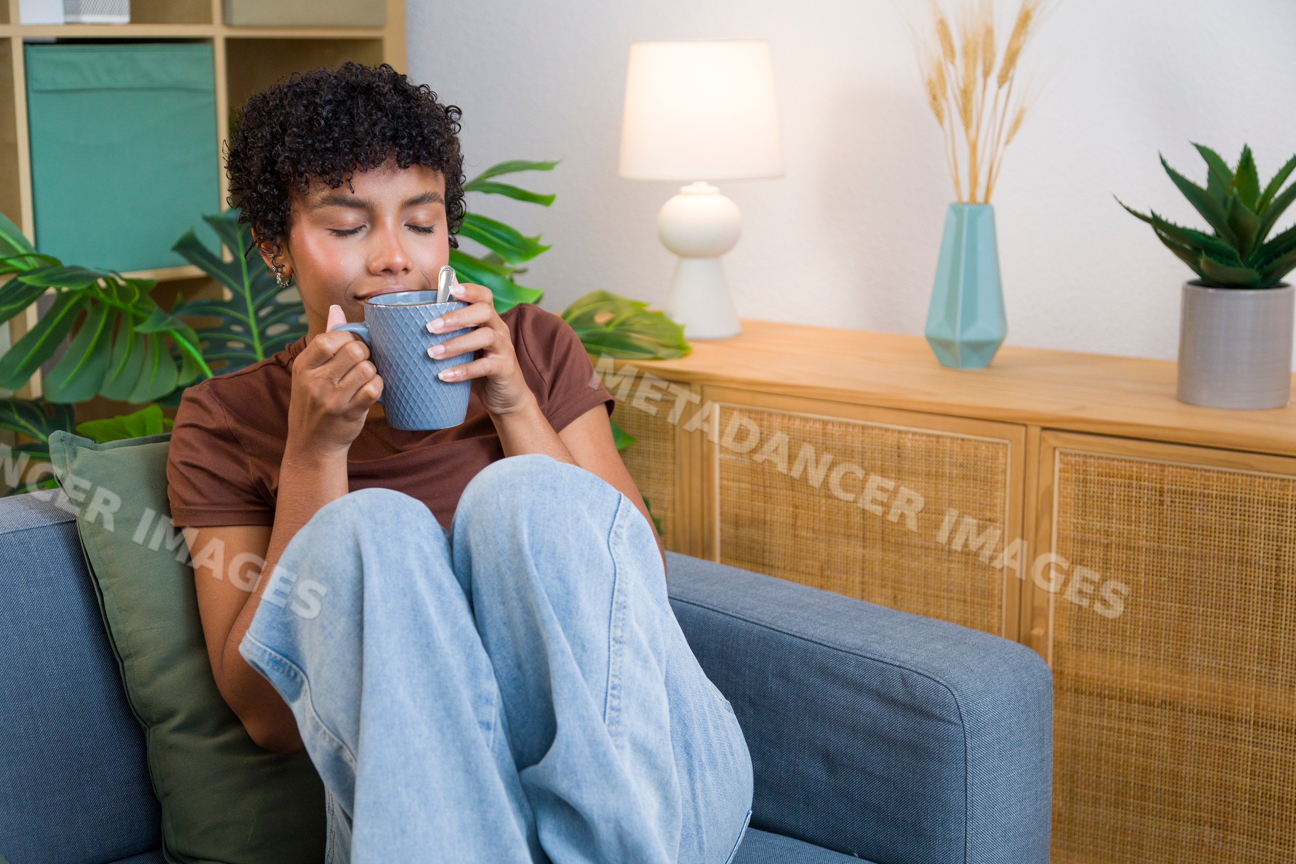 Young African American woman relaxing with blue mug on grey sofa