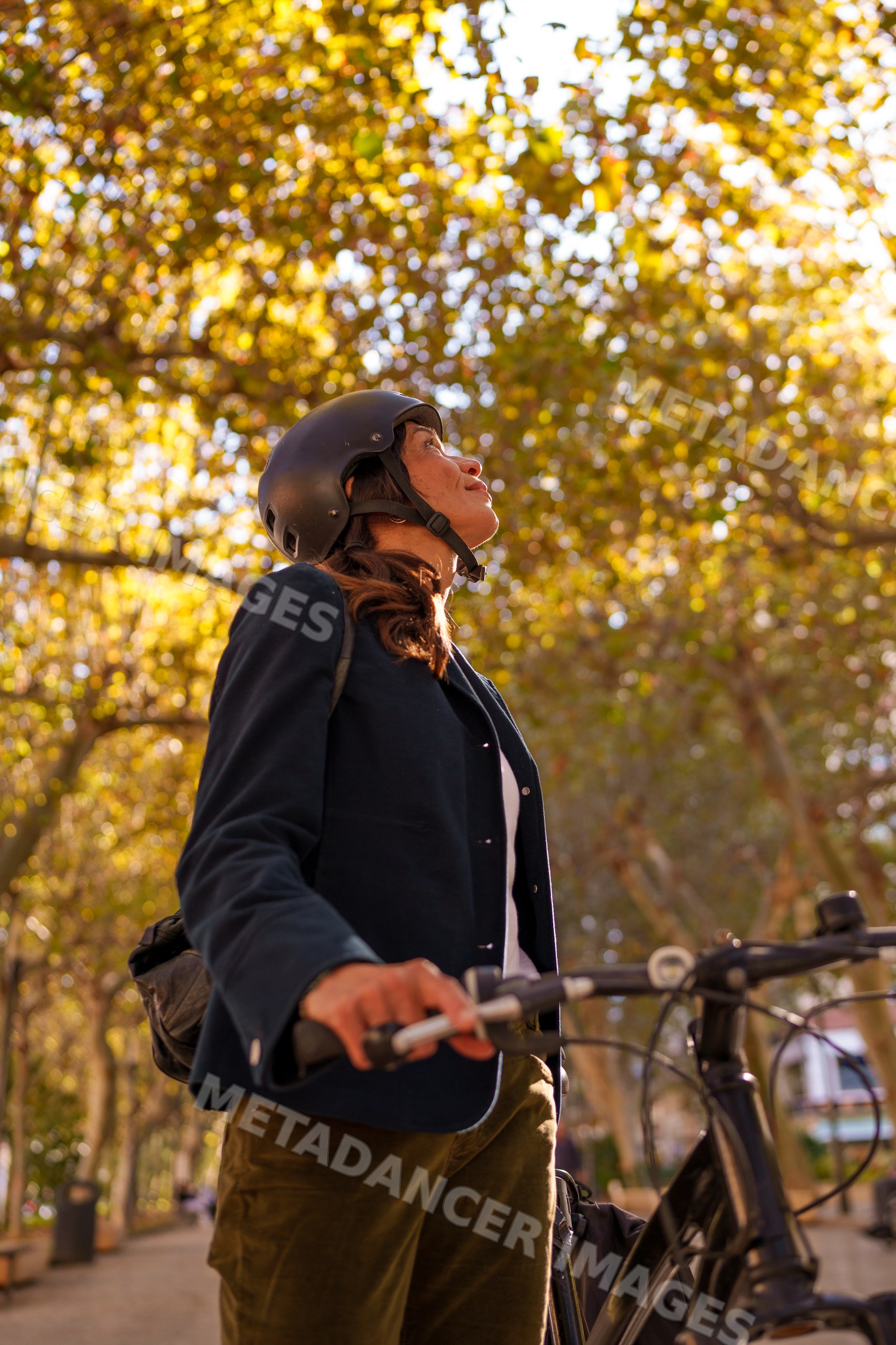 Hispanic woman standing by bicycle in autumn park in Málaga