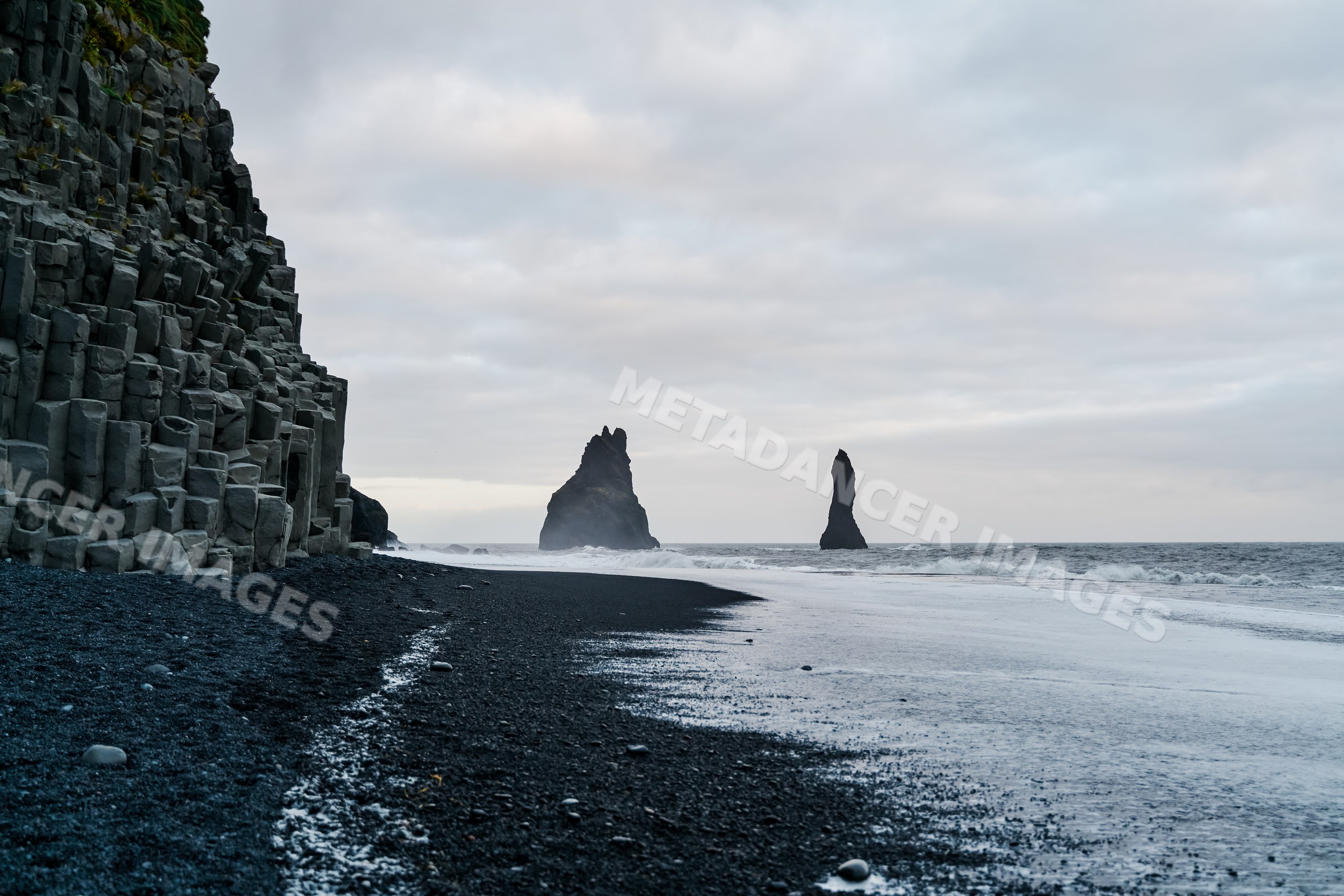 Basalt columns rise along a black sand beach with ocean waves