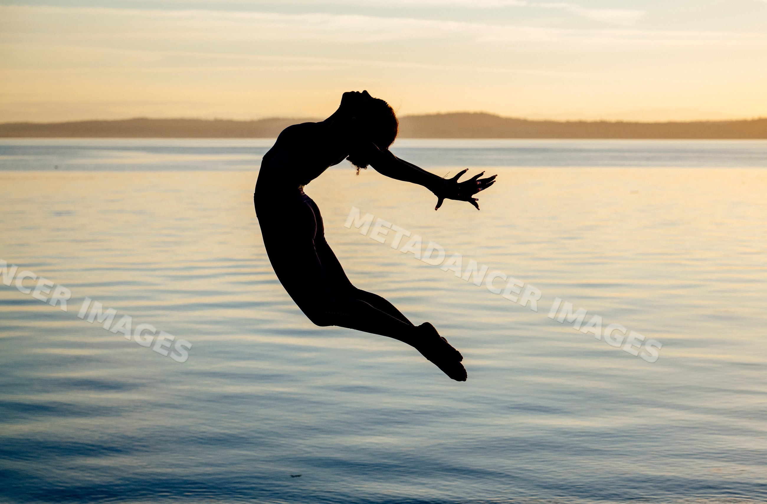 Hispanic woman performing acrobatic jump silhouette over lake