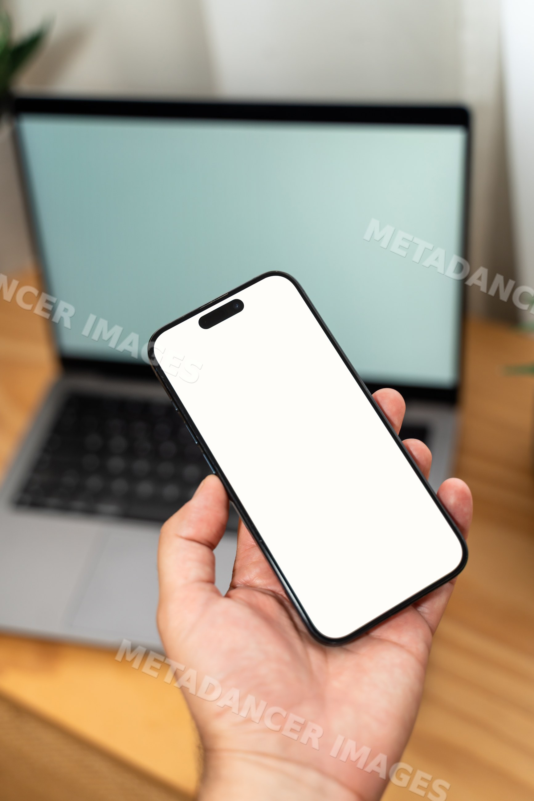 Smartphone held in hand in front of laptop on desk