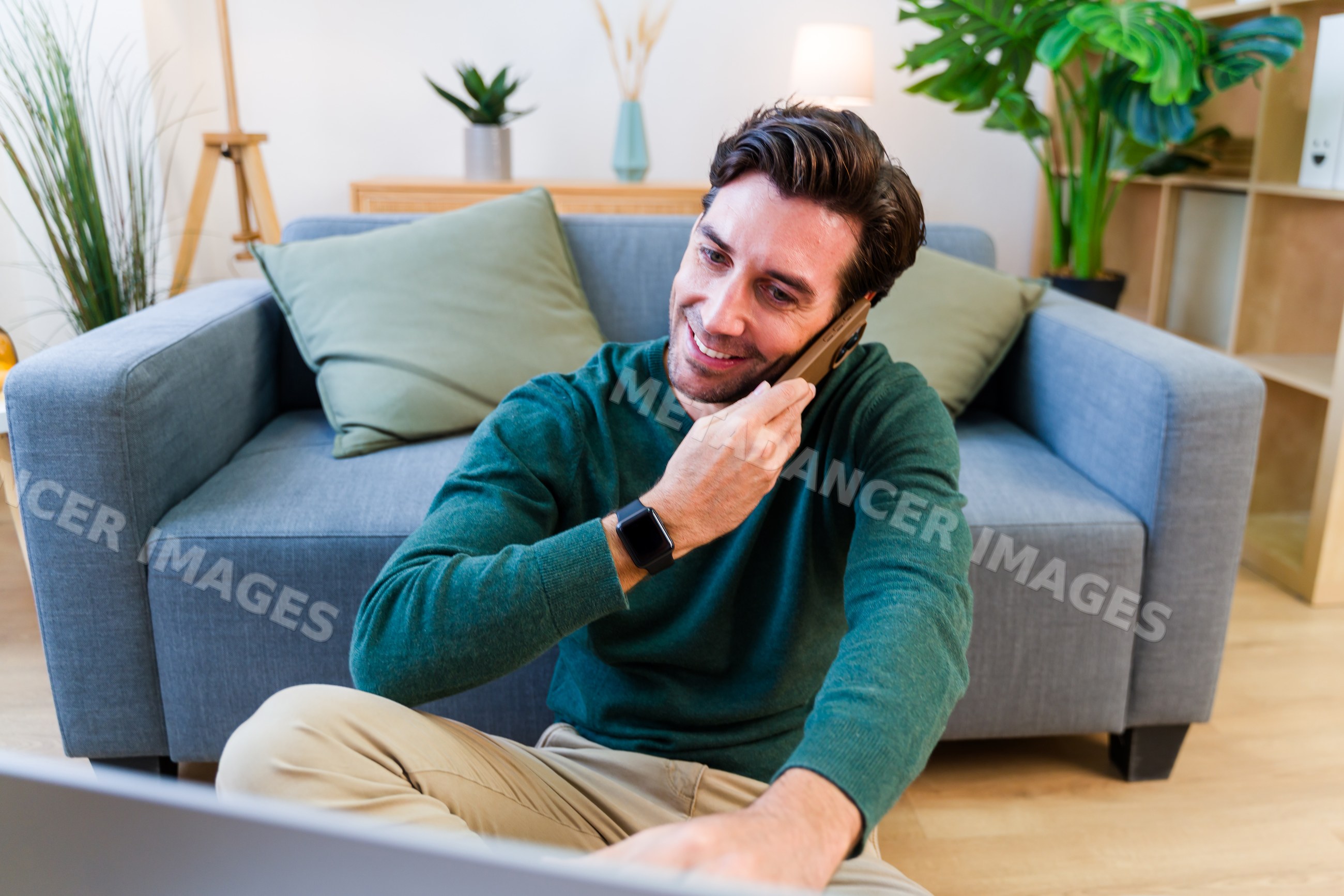 White man sitting on floor calling on mobile phone in living room