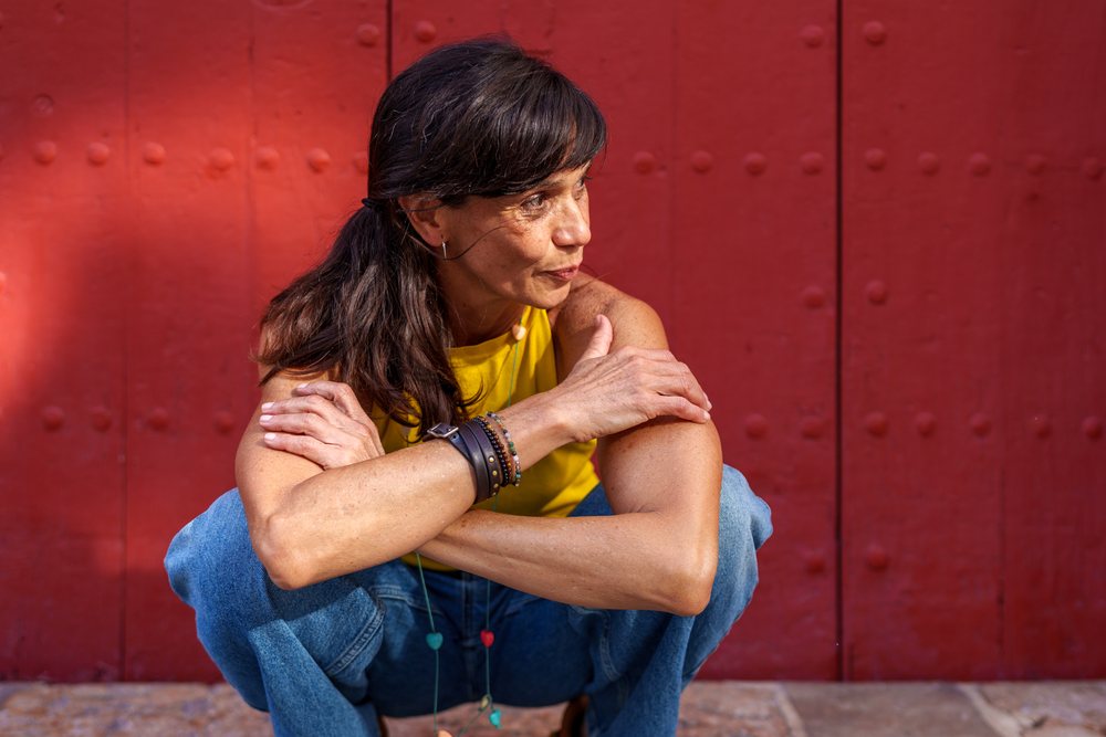 Hispanic woman crouching outdoors against red wall