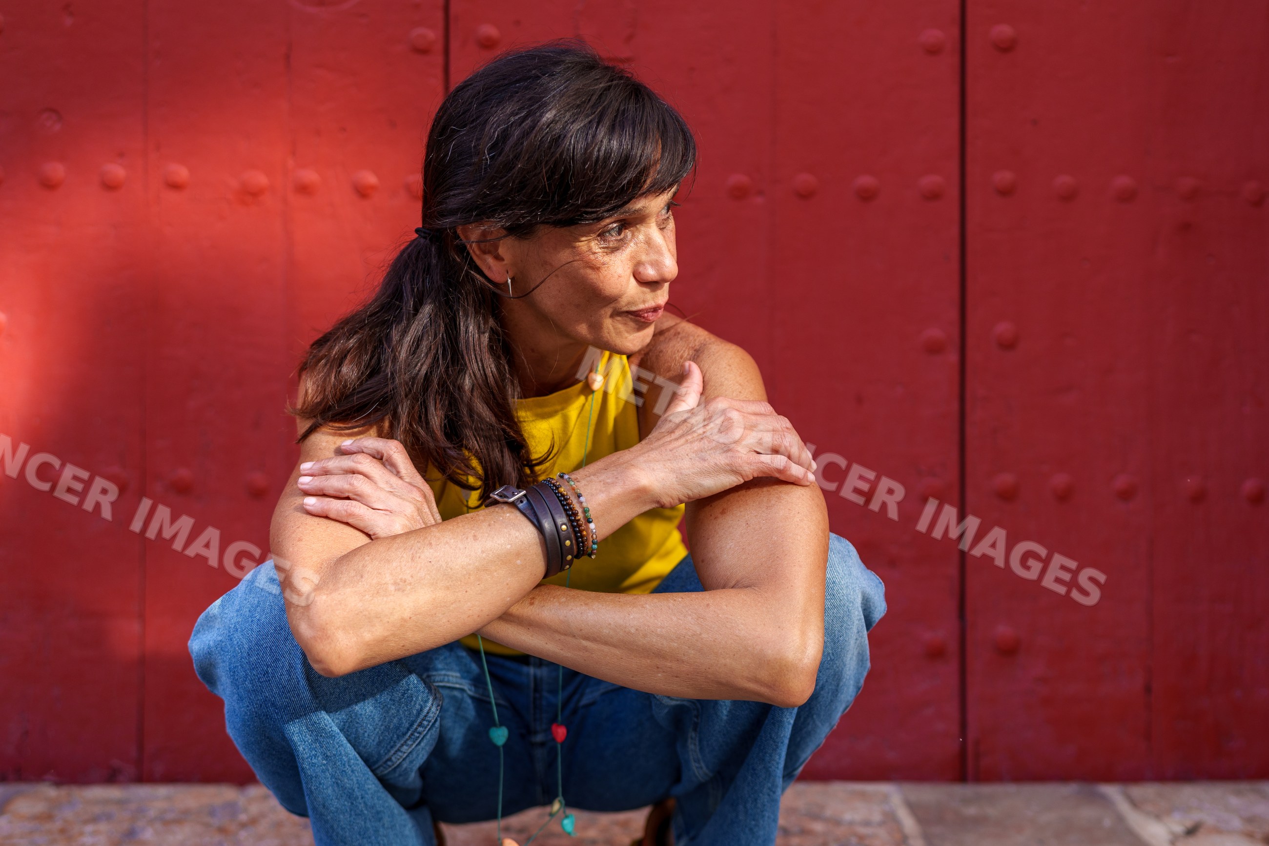 Hispanic woman crouching outdoors against red wall