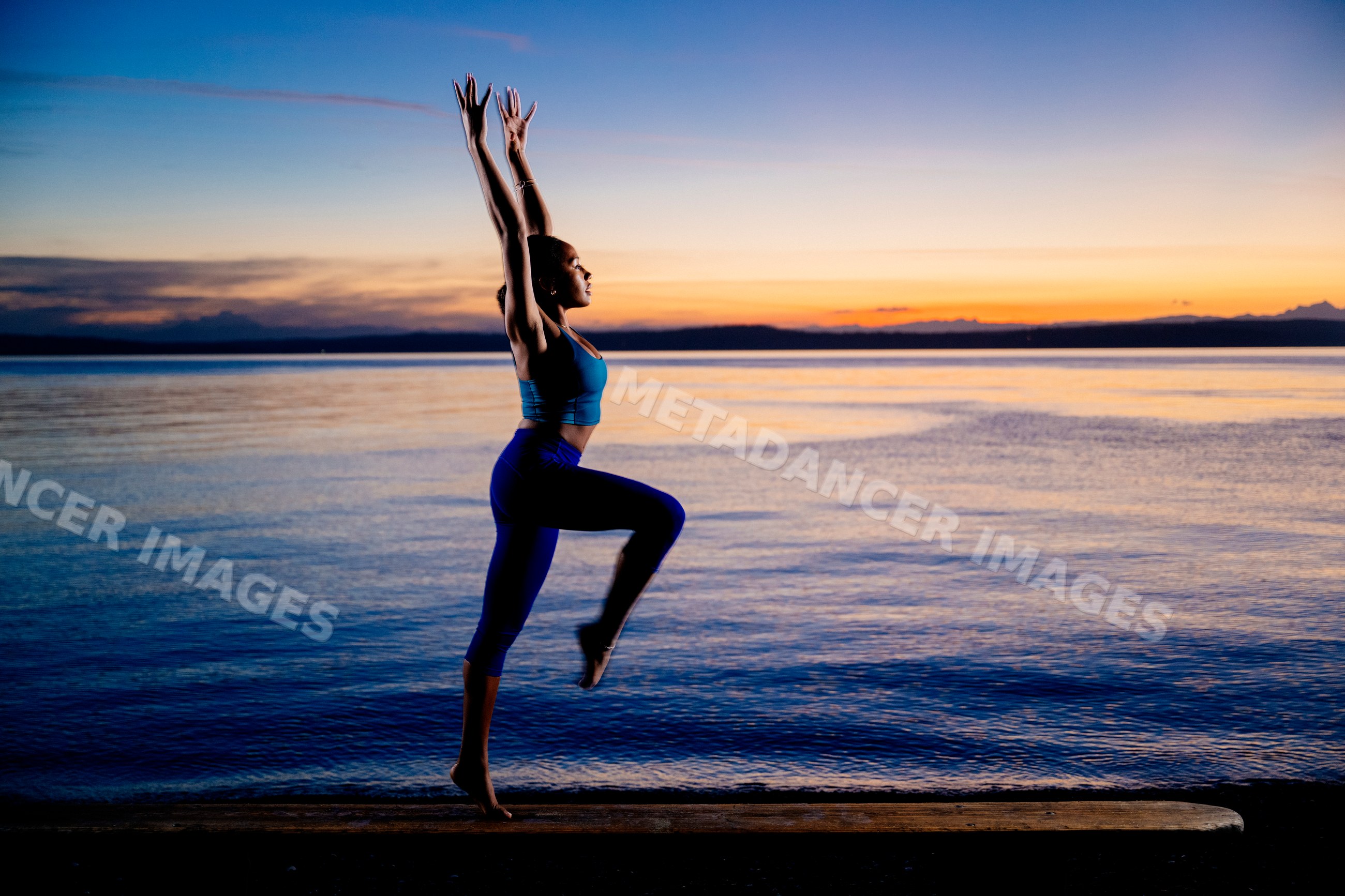 Hispanic woman performing an acrobatic yoga pose on a shore