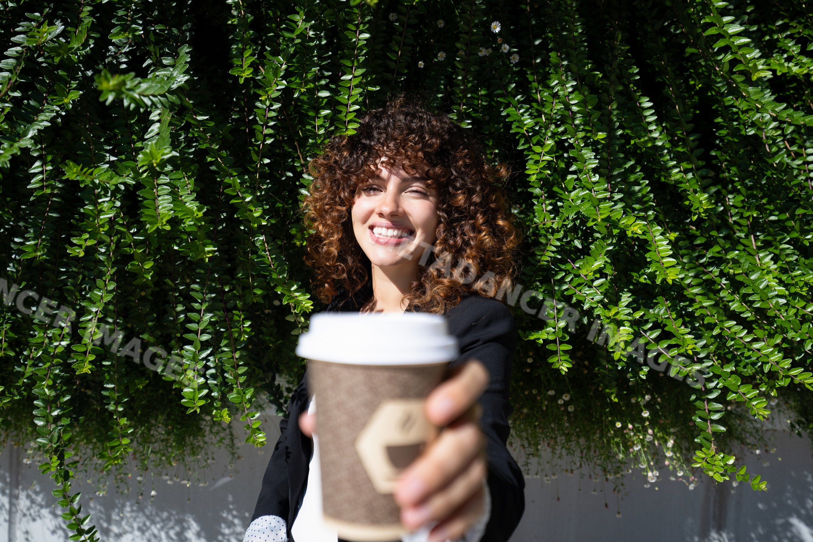 White woman holding takeaway coffee cup outdoors with green foliage