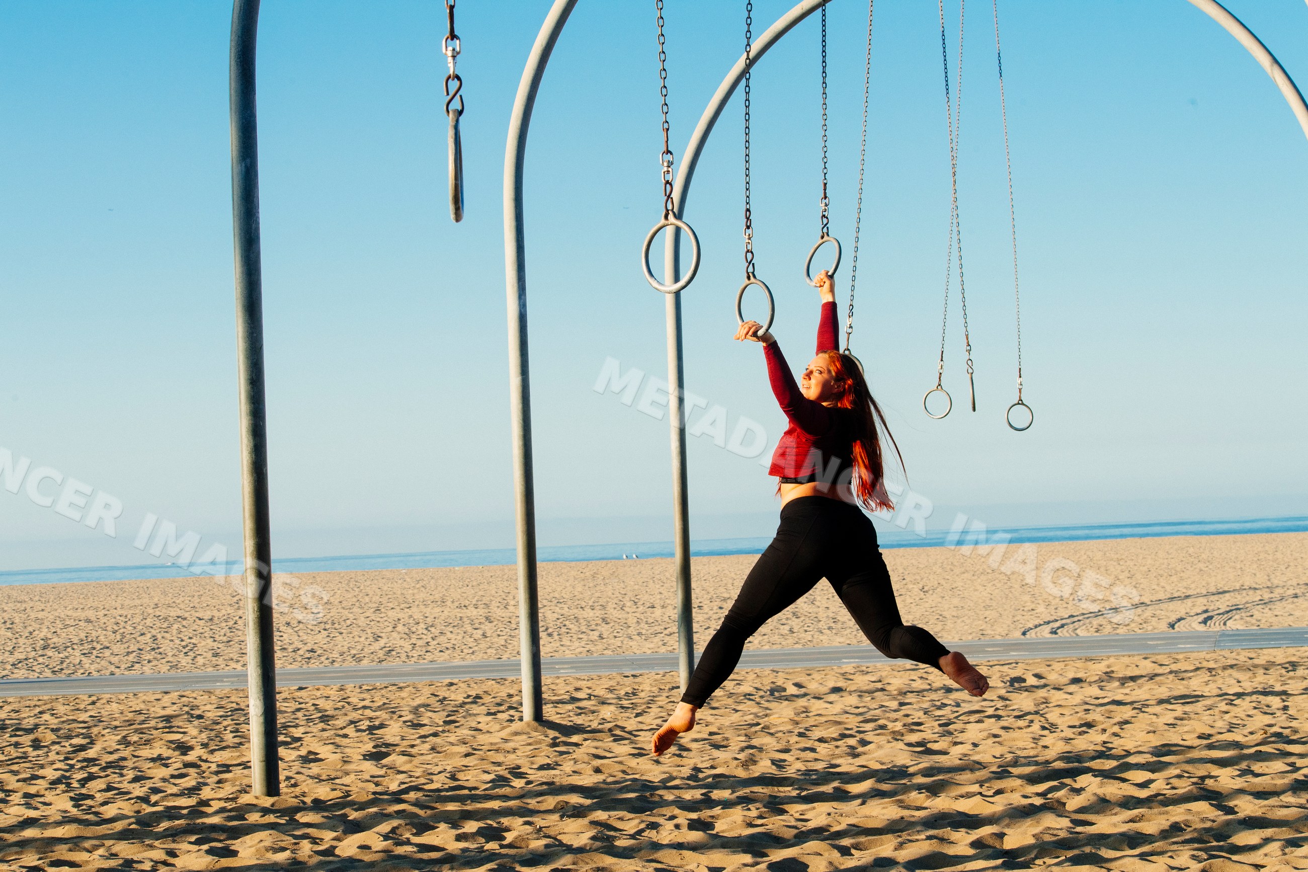 White woman swinging on gymnastic rings on beach in a beach