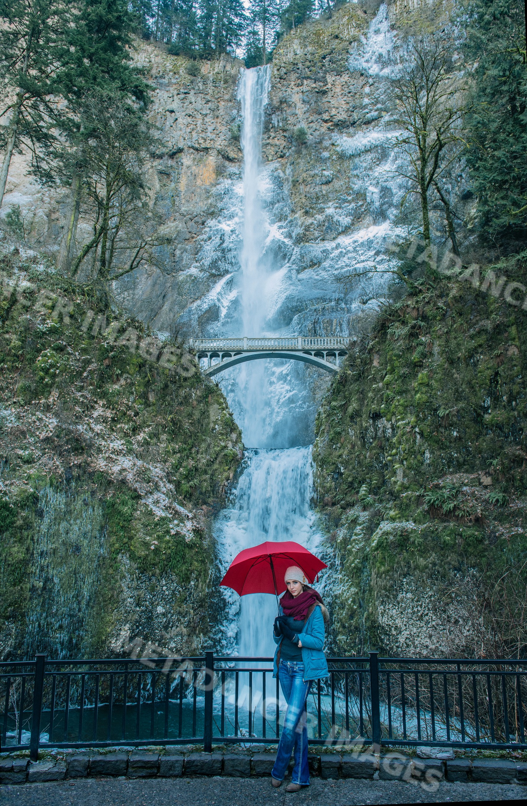 White woman with red umbrella at two-tiered multnomah falls and bridge