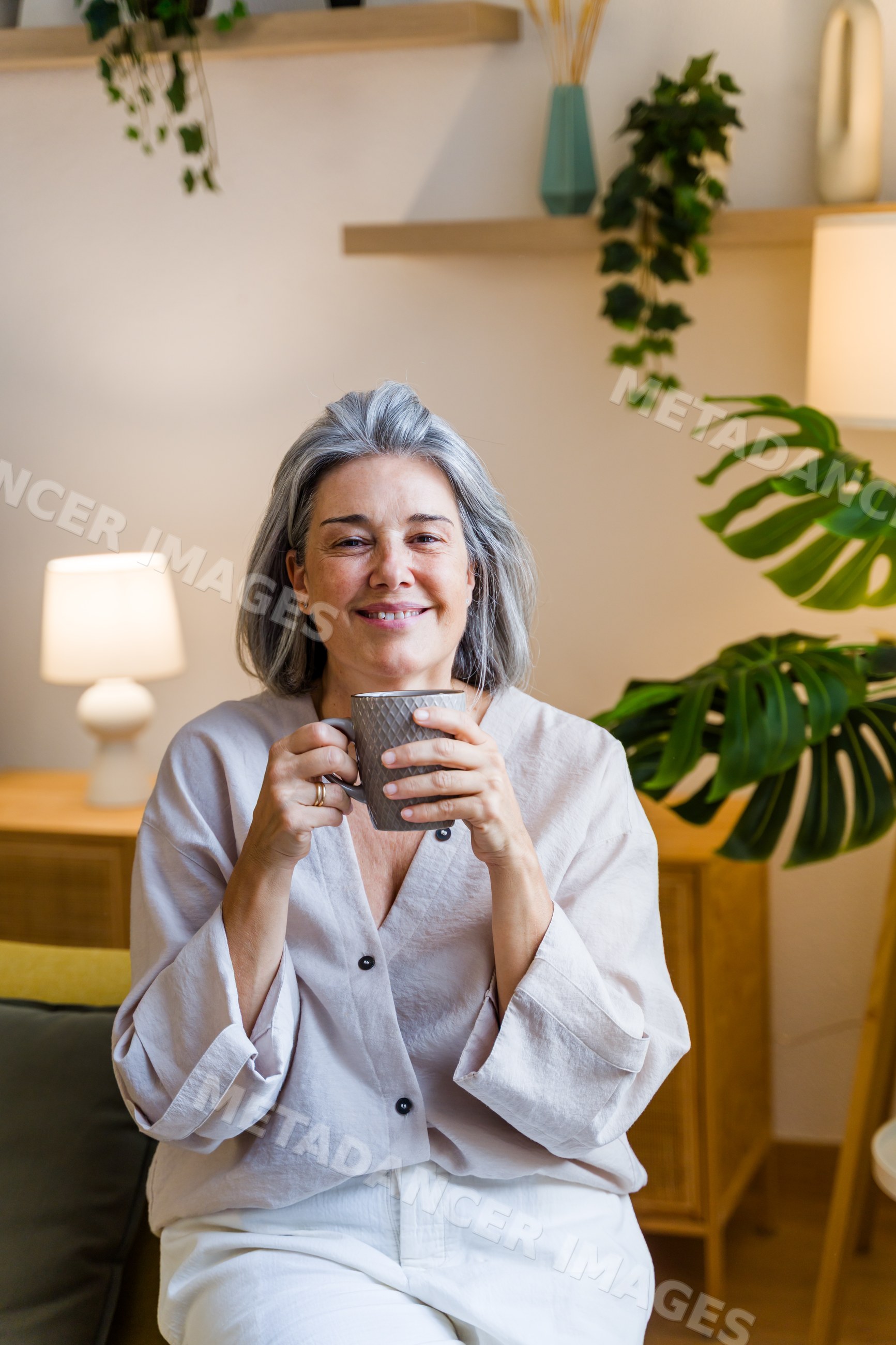 Middle-aged white woman holding gray cup and smiling living room