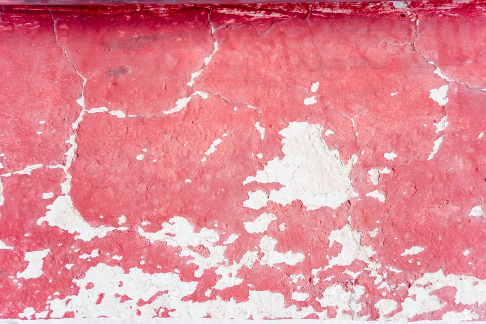 Weathered wall with peeling red paint and surface cracks