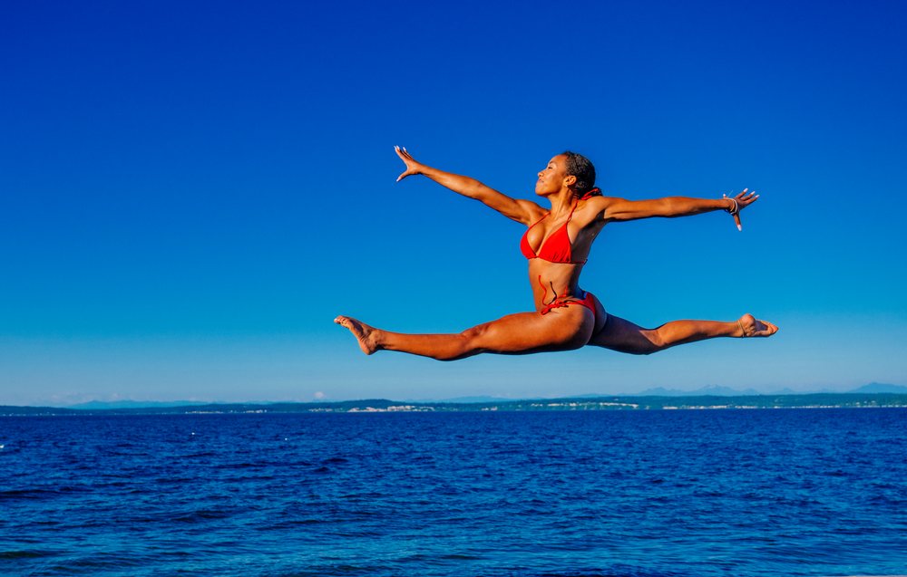 Woman in red swimsuit jumping in a split leap over the ocean