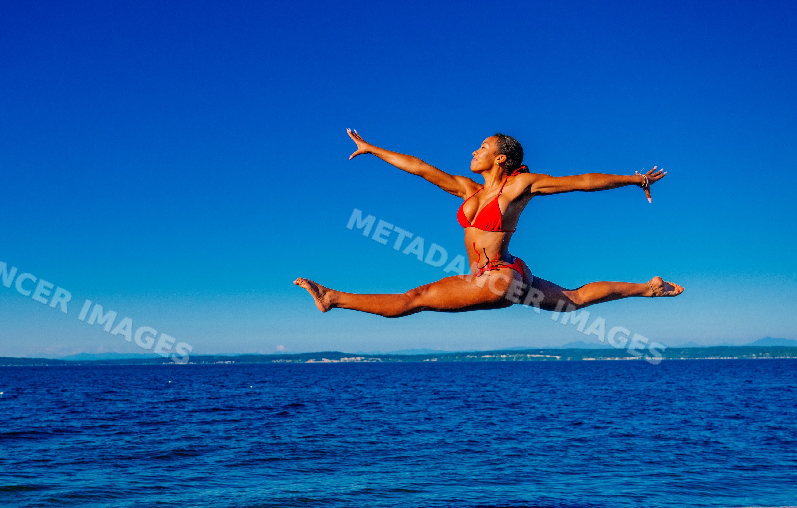 Woman in red swimsuit jumping in a split leap over the ocean