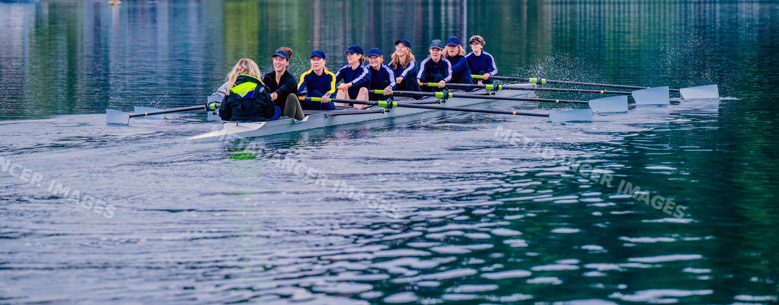 A white women's rowing team practices together on a calm lake