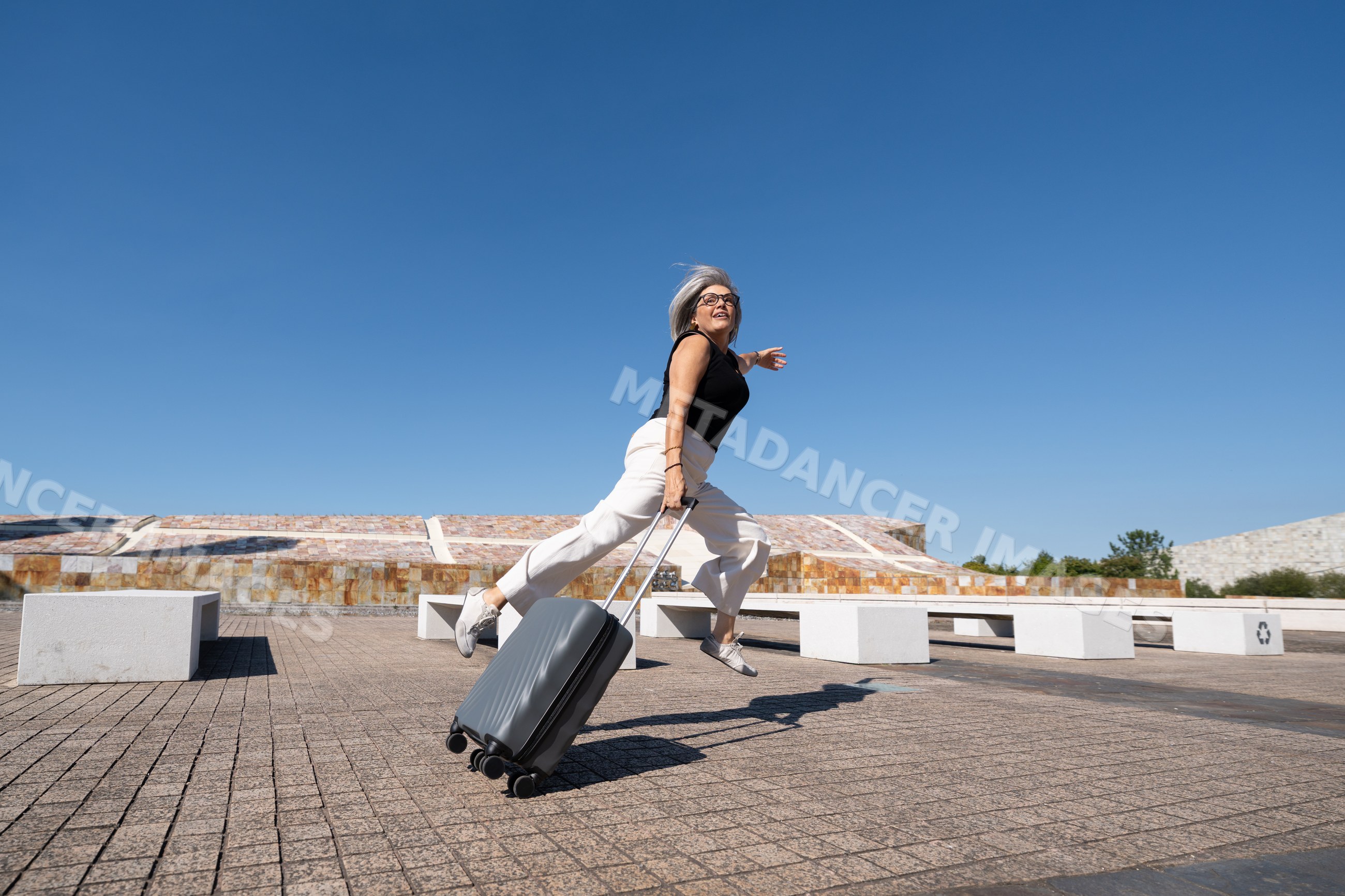 White woman jumping with suitcase on a sunny plaza